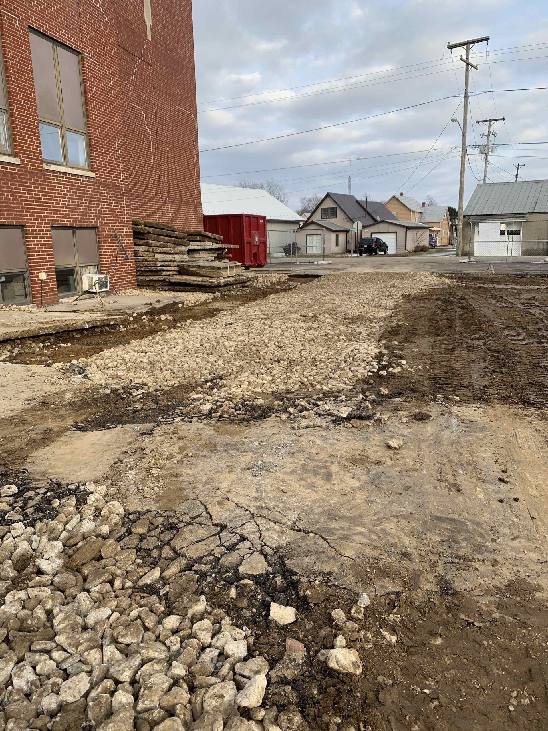 Street construction site with exposed dirt and gravel, next to a red brick building.