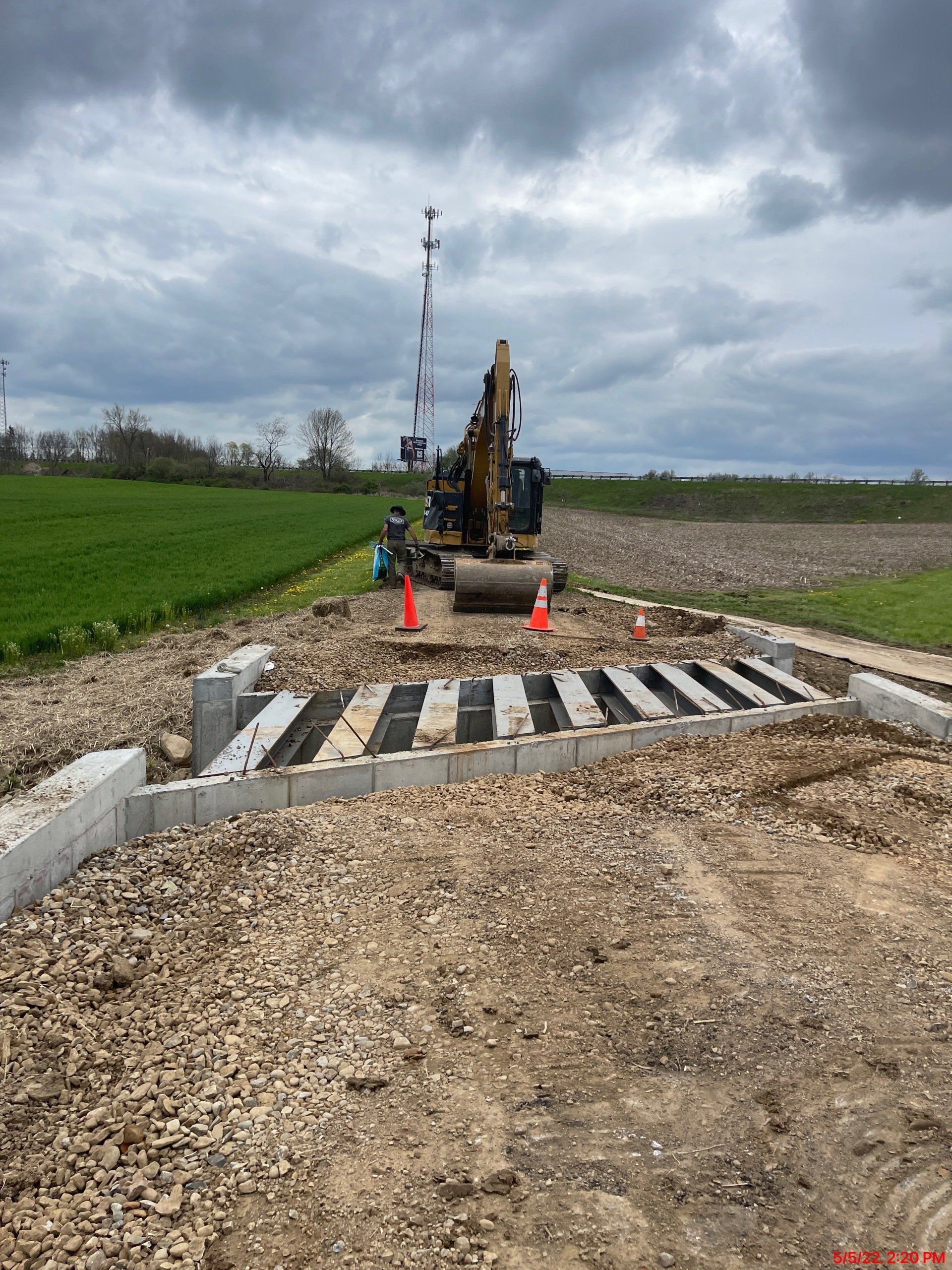 Construction site: Excavator near a concrete and gravel railway crossing under a cloudy sky.