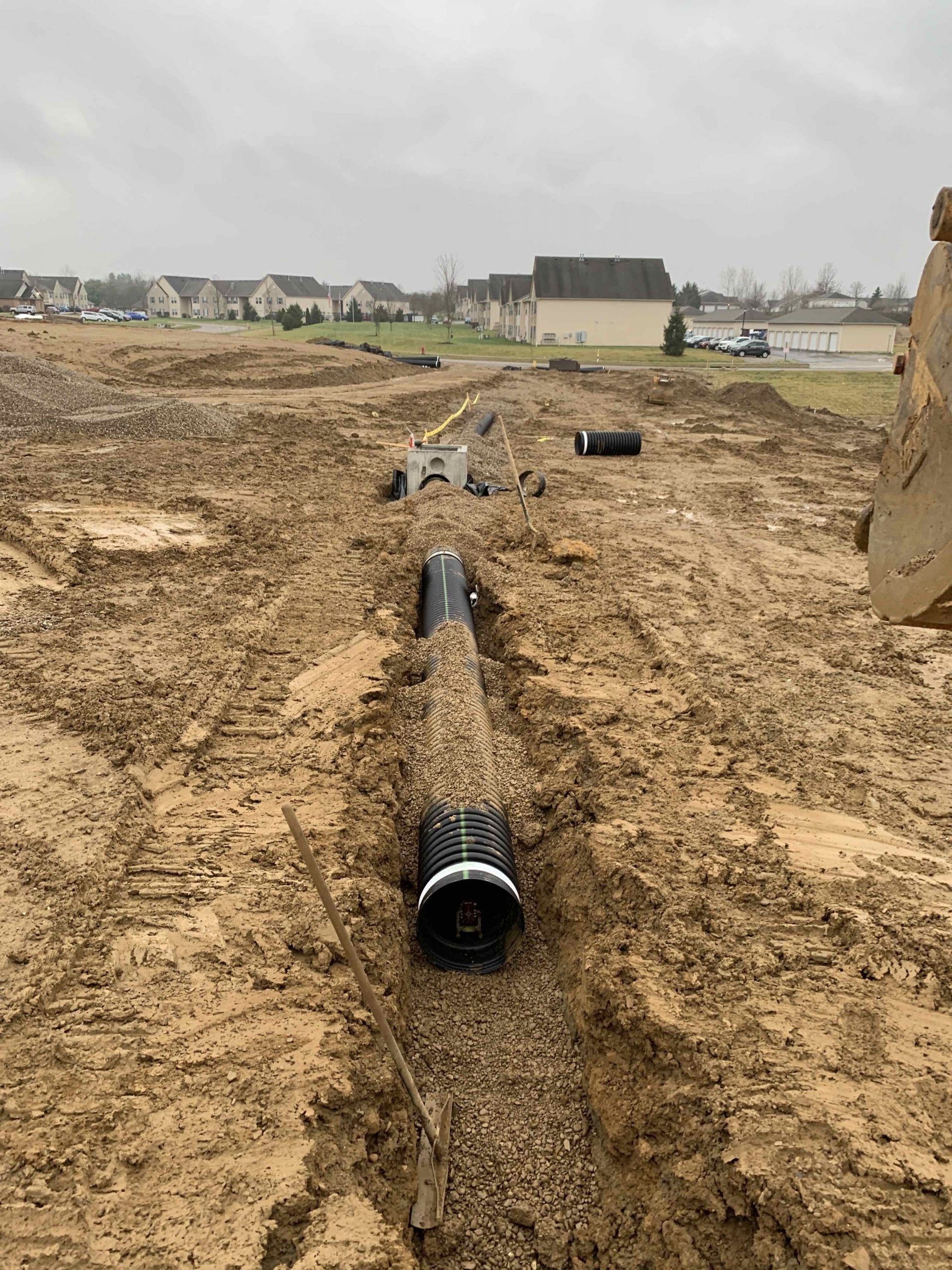 Black drainage pipes laid in a trench at a construction site. Houses in the background.