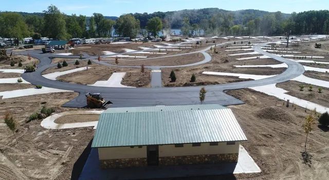 Aerial view of a campsite with paved roads, individual plots, and a green-roofed building.