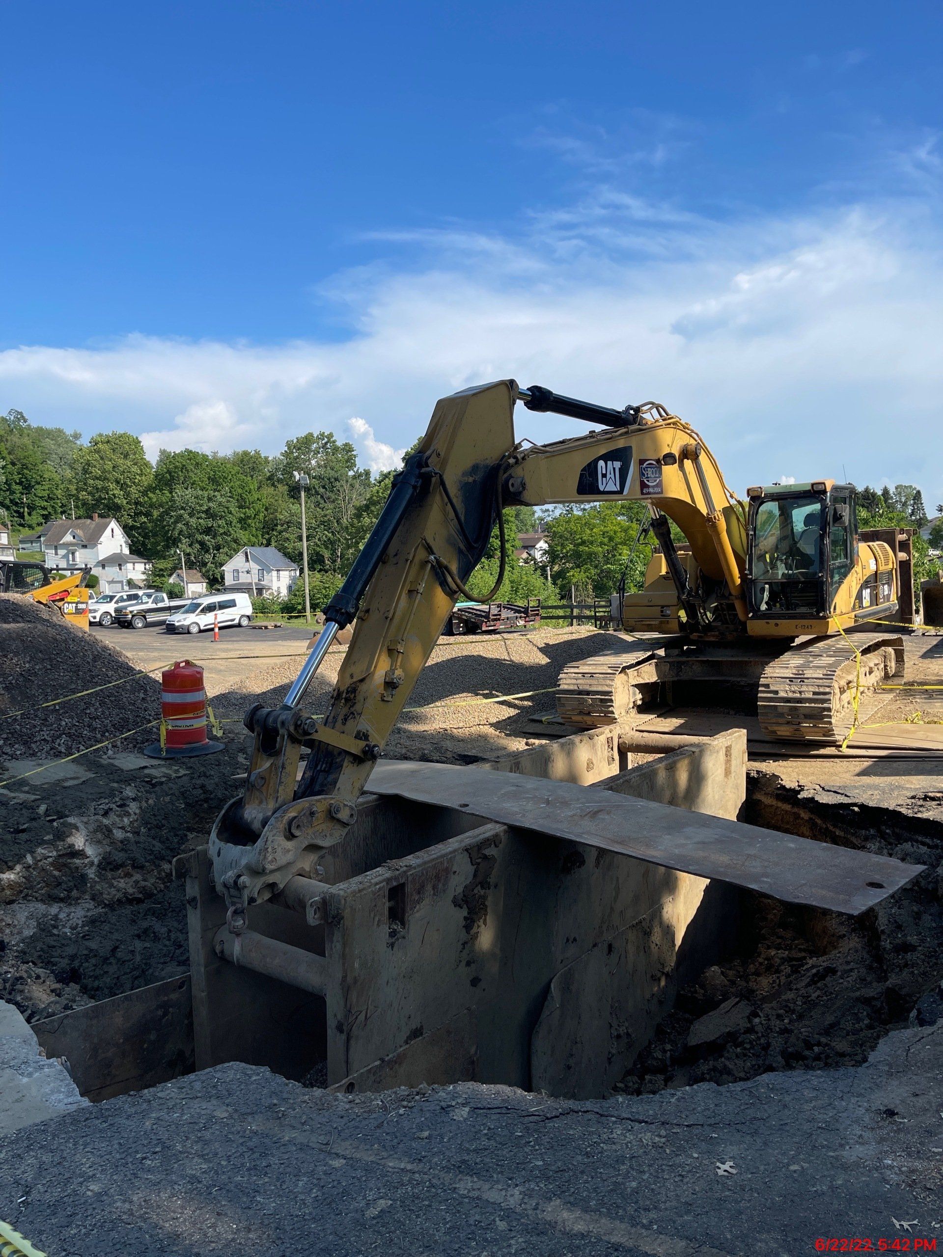 Yellow excavator working in a construction site, digging into a large hole, blue sky.