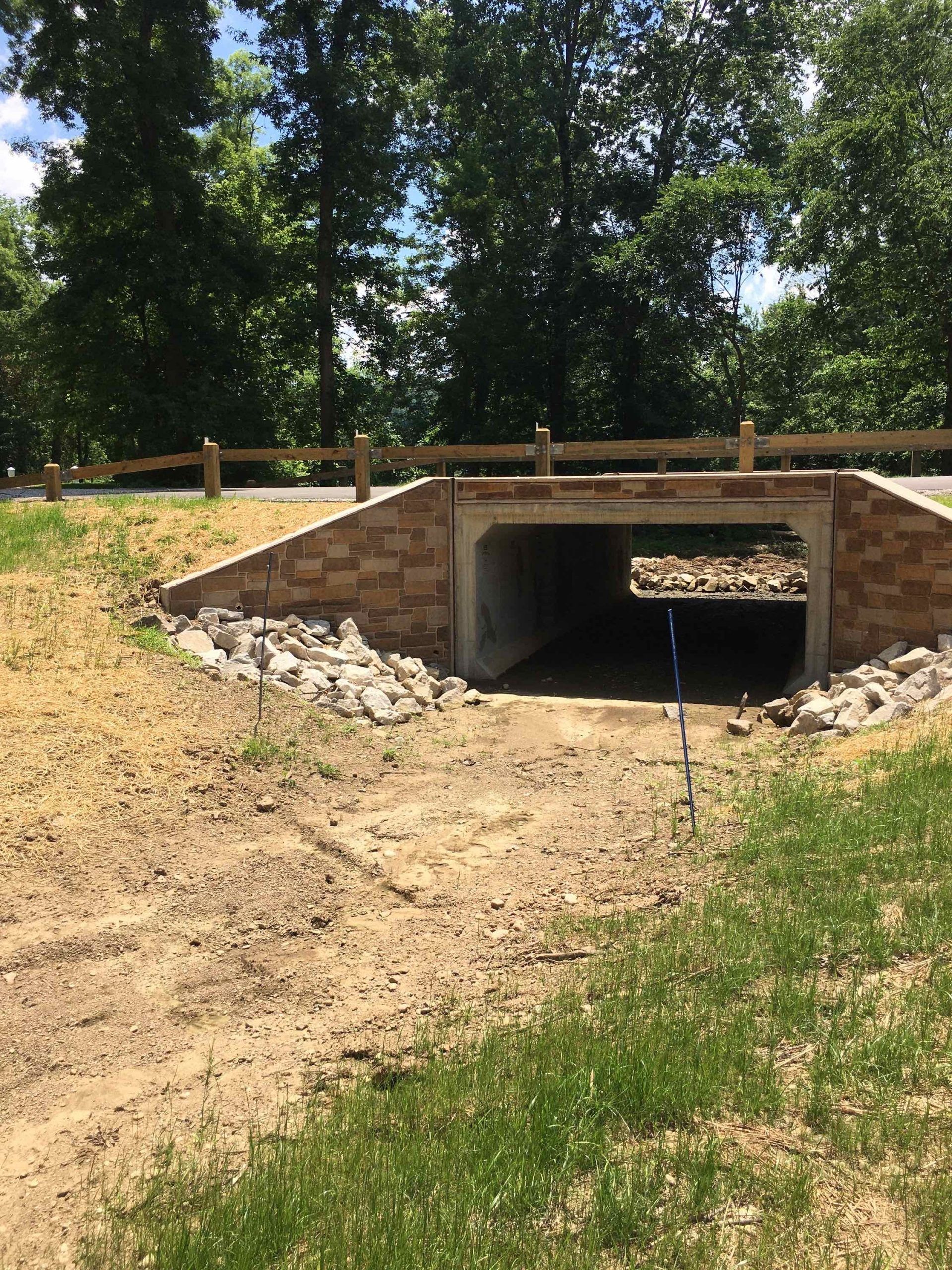 A small tunnel under a road, constructed of brick, surrounded by grass and dirt.