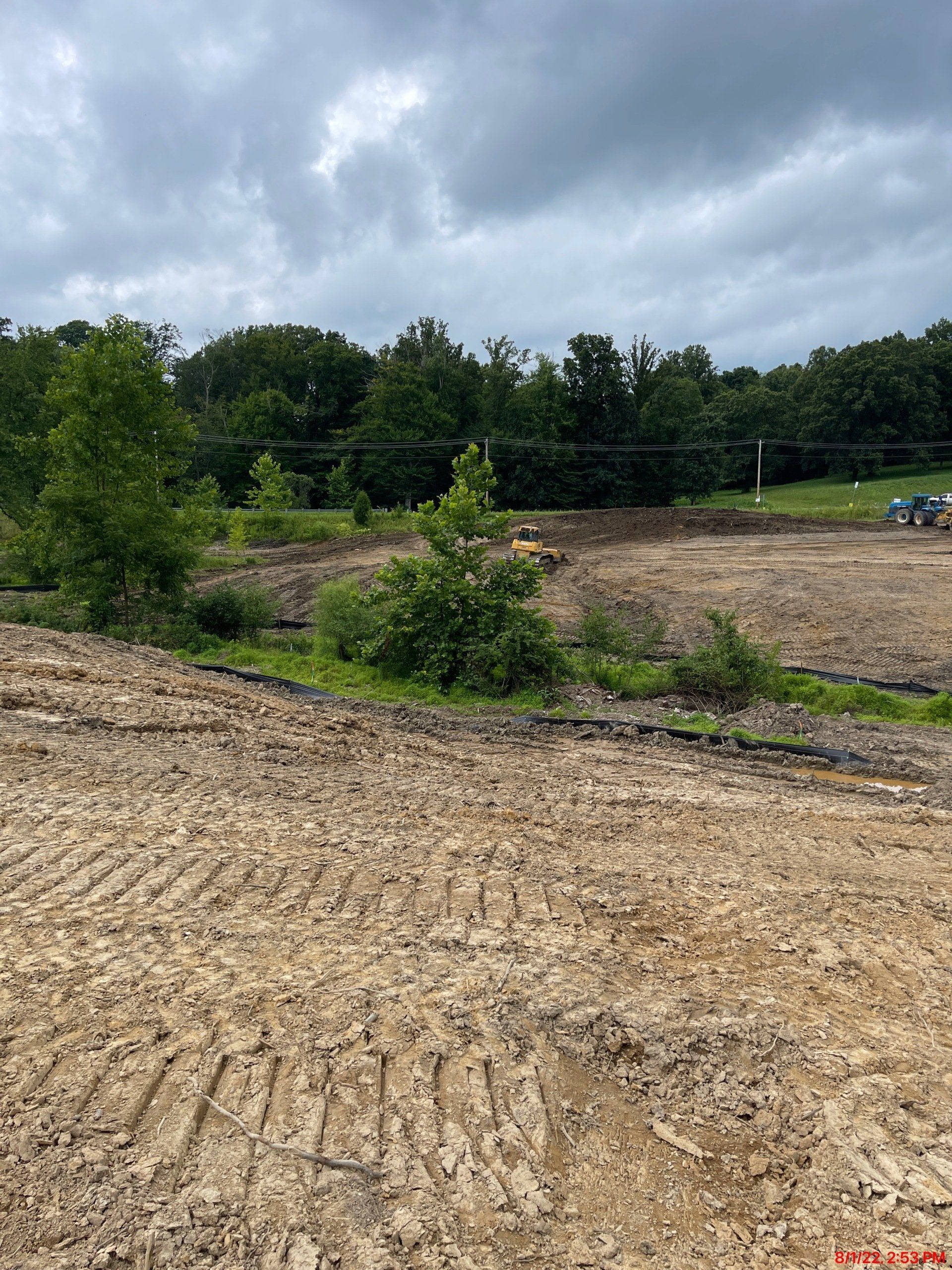 Construction site with exposed dirt and a few small trees, under an overcast sky.