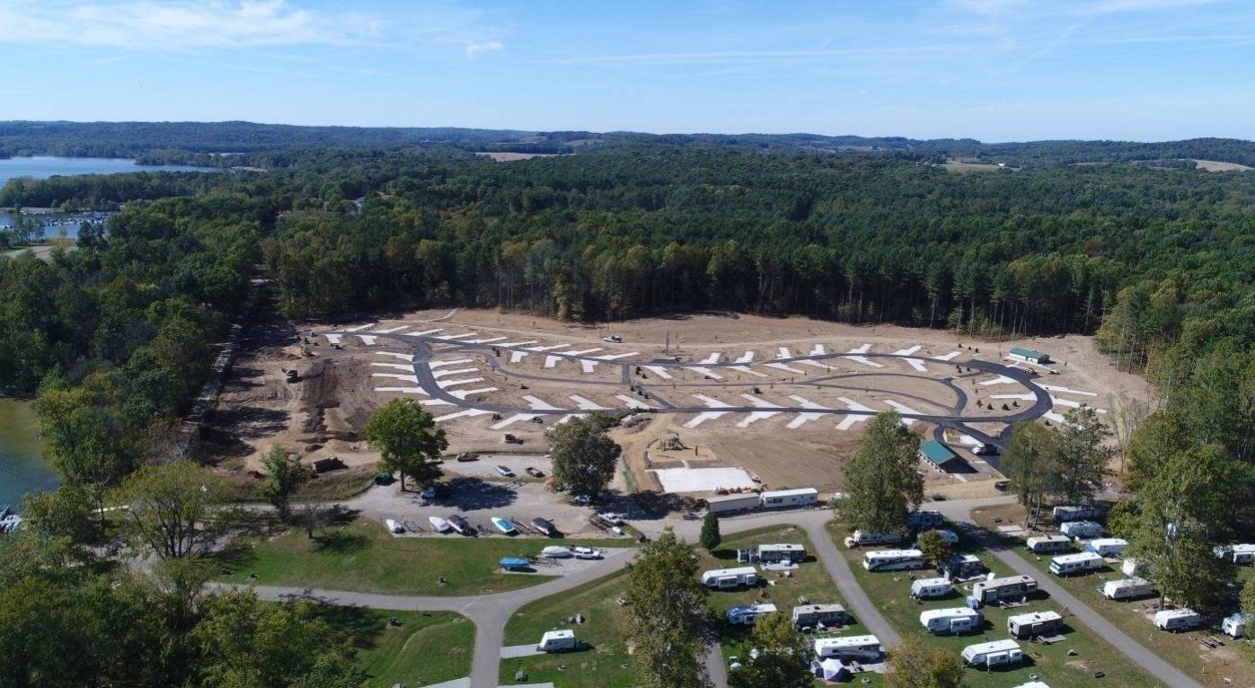 Aerial view of a campground with RVs, trees, and construction, on a sunny day.