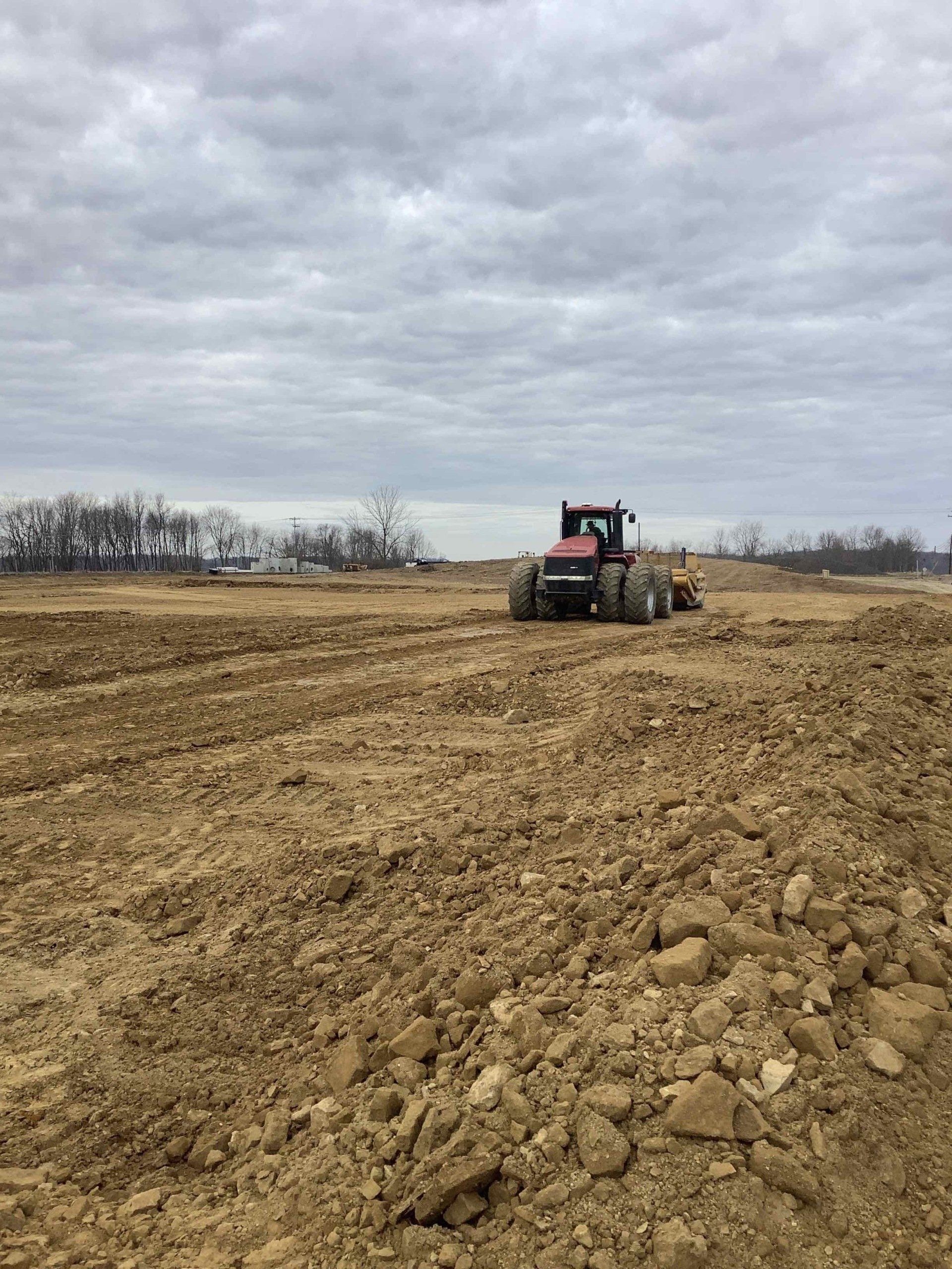 Red tractor plowing a dirt field under a cloudy sky.