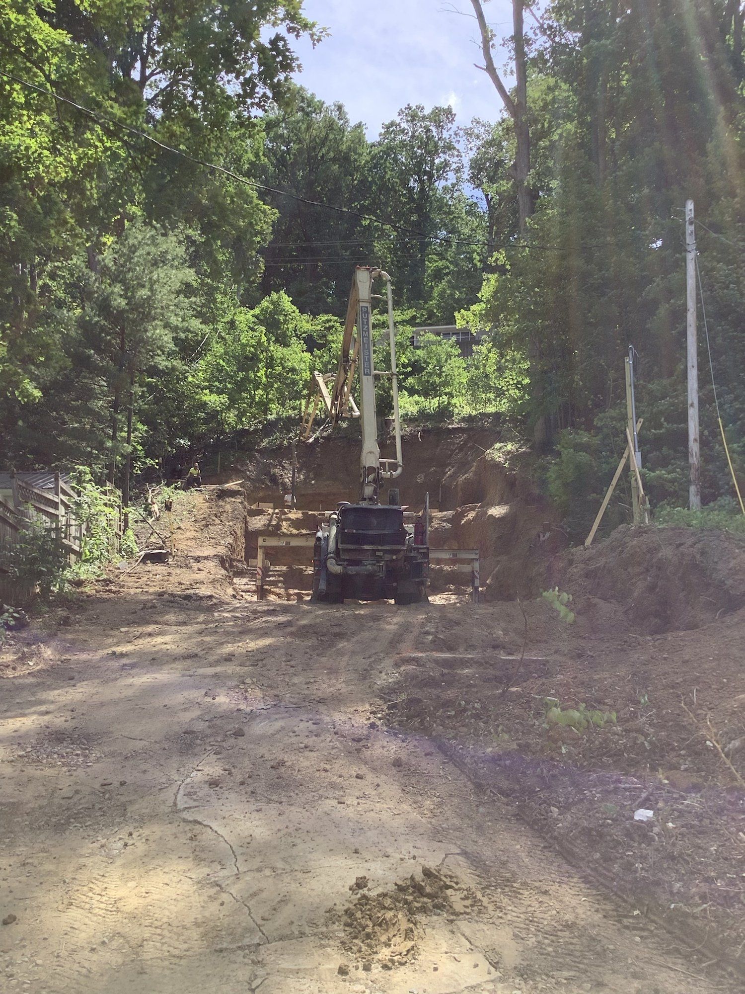 A concrete pump truck on a dirt road, reaching toward a forested area.