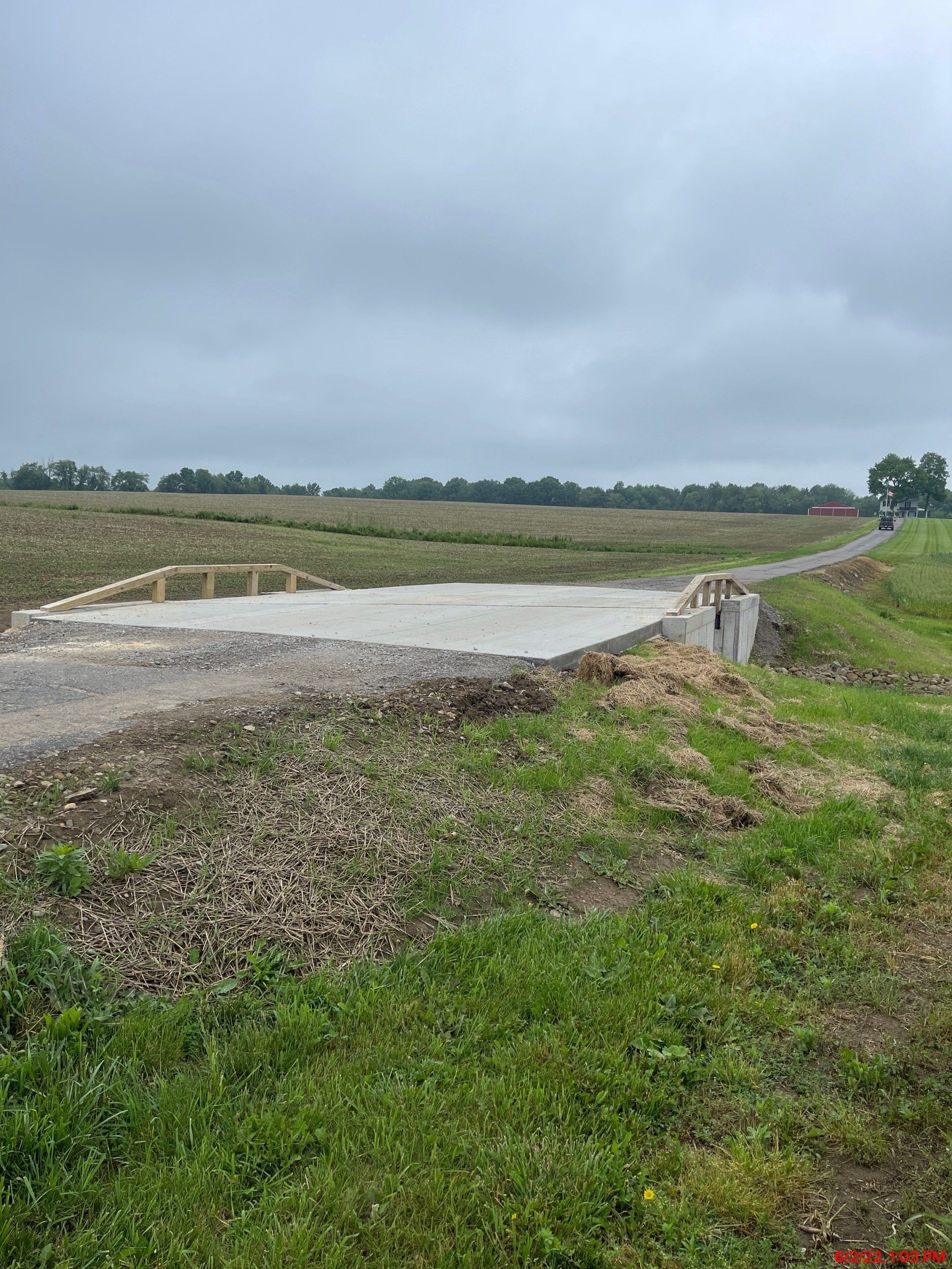 Gravel road leading to a concrete pad, likely a foundation, in a field under a cloudy sky.