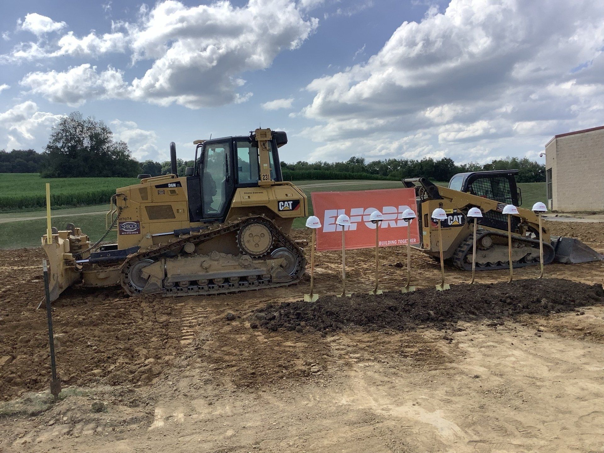 Two yellow bulldozers on a construction site; blue sky and a sign are in the background.