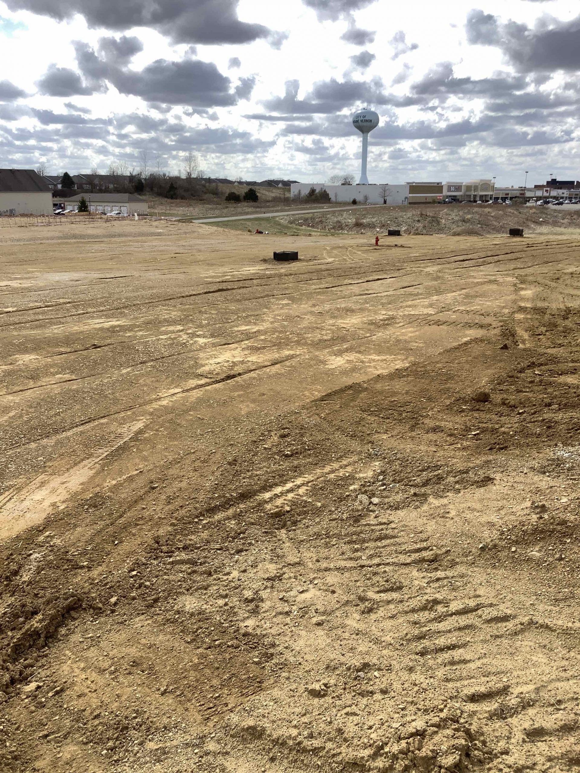 Barren dirt field with distant water tower and cloudy sky.