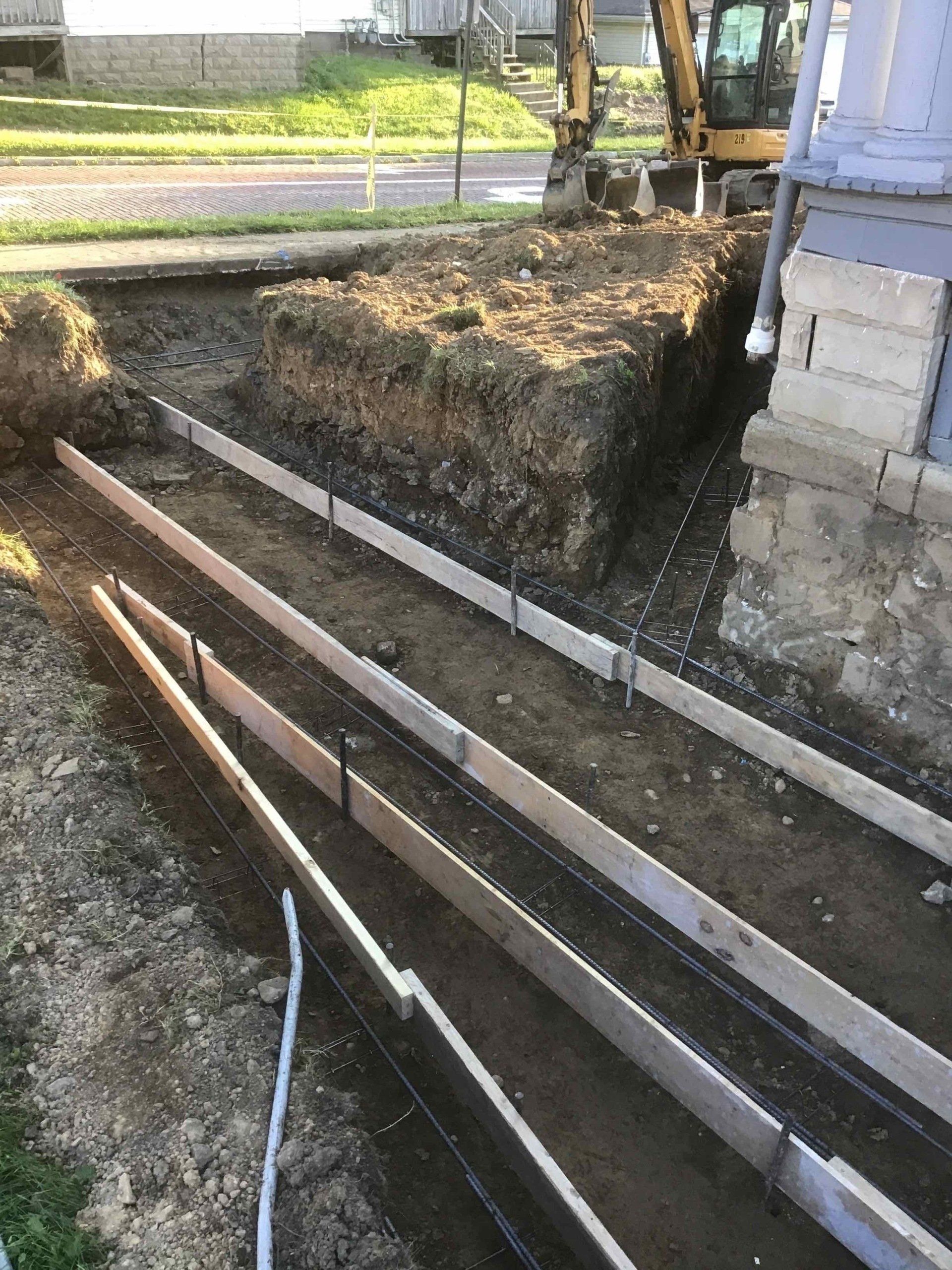 Construction site with concrete forms set in trench. Backhoe and building in the background.