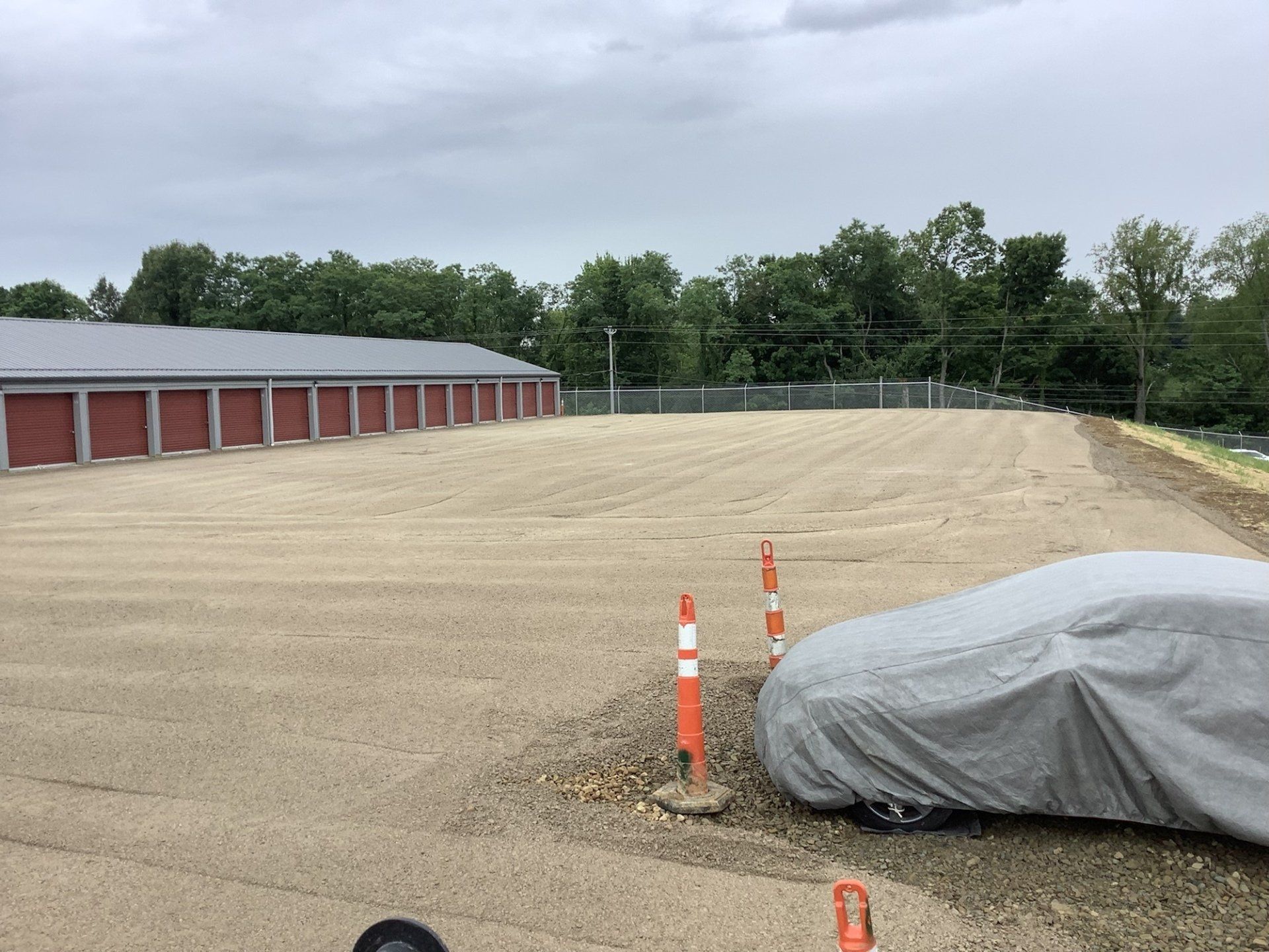 Storage units, gravel lot, covered car, and orange safety markers.