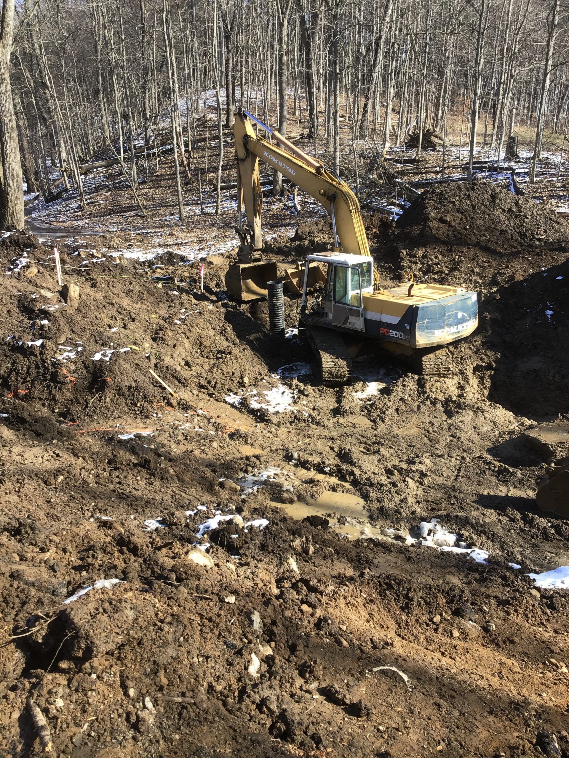 Excavator in muddy terrain, surrounded by trees.