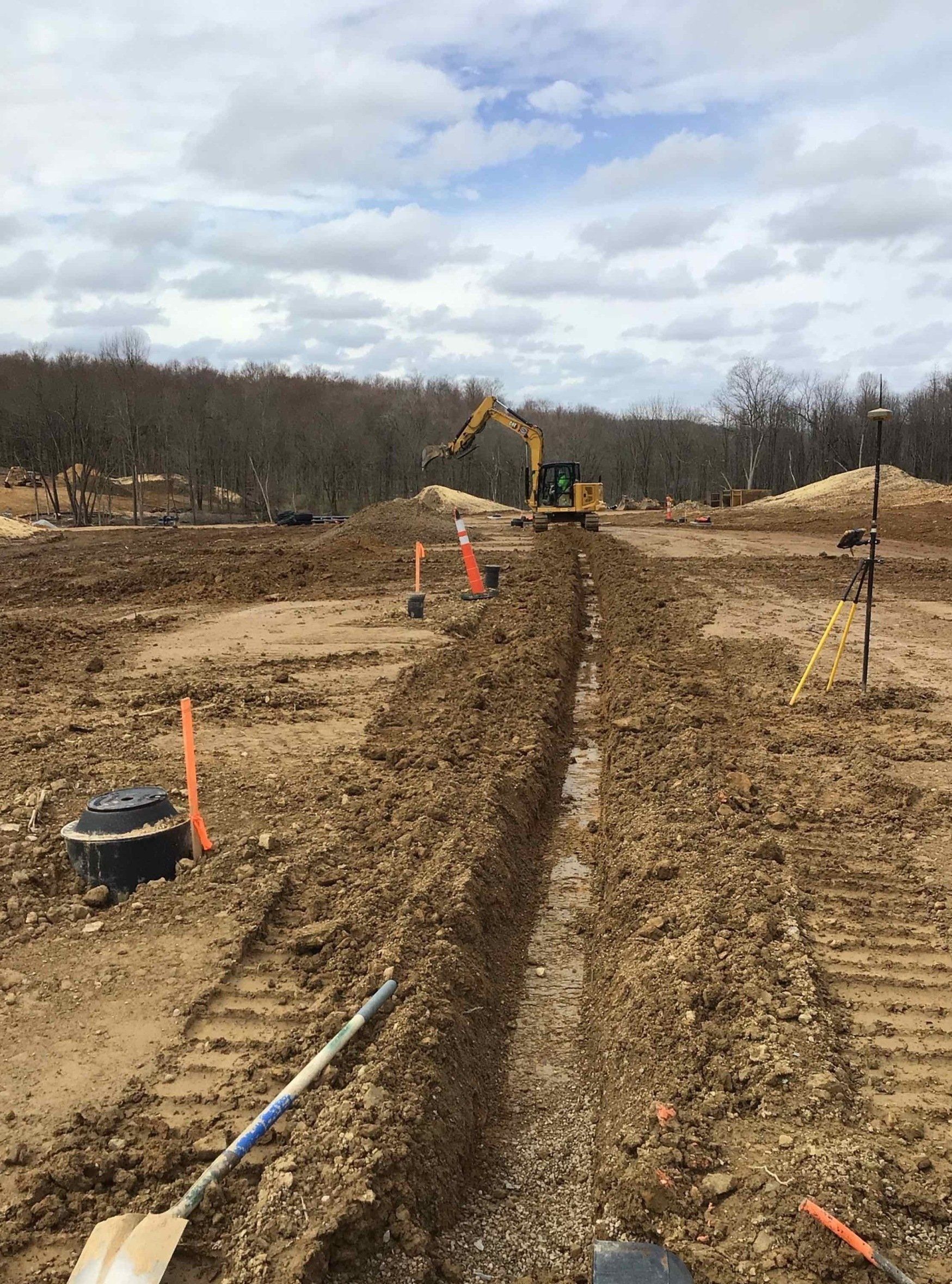 Construction site: excavator digging trench in muddy field, overcast sky.