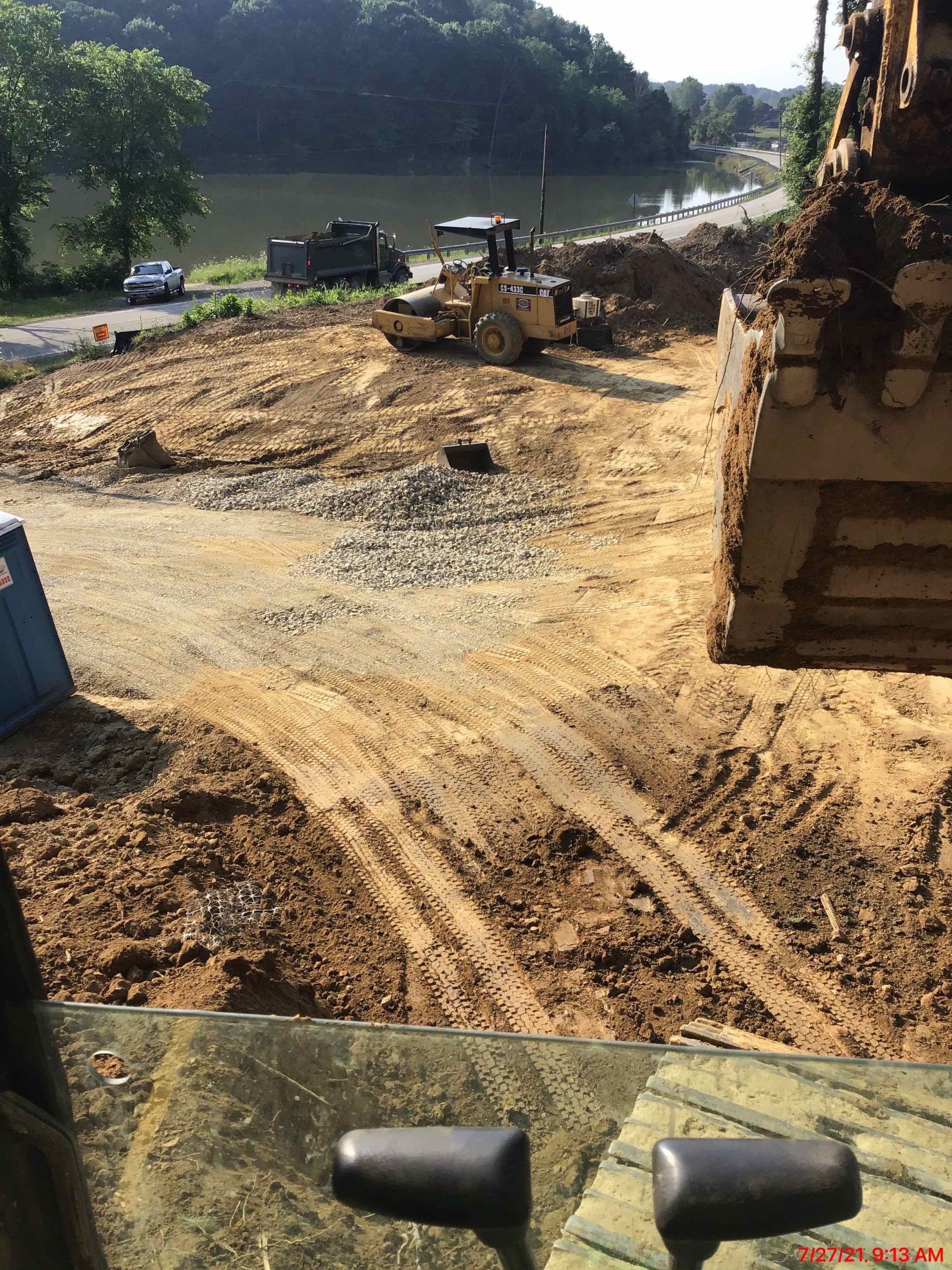 Construction site with heavy machinery, a yellow bulldozer, and earth-moving operations near a river.