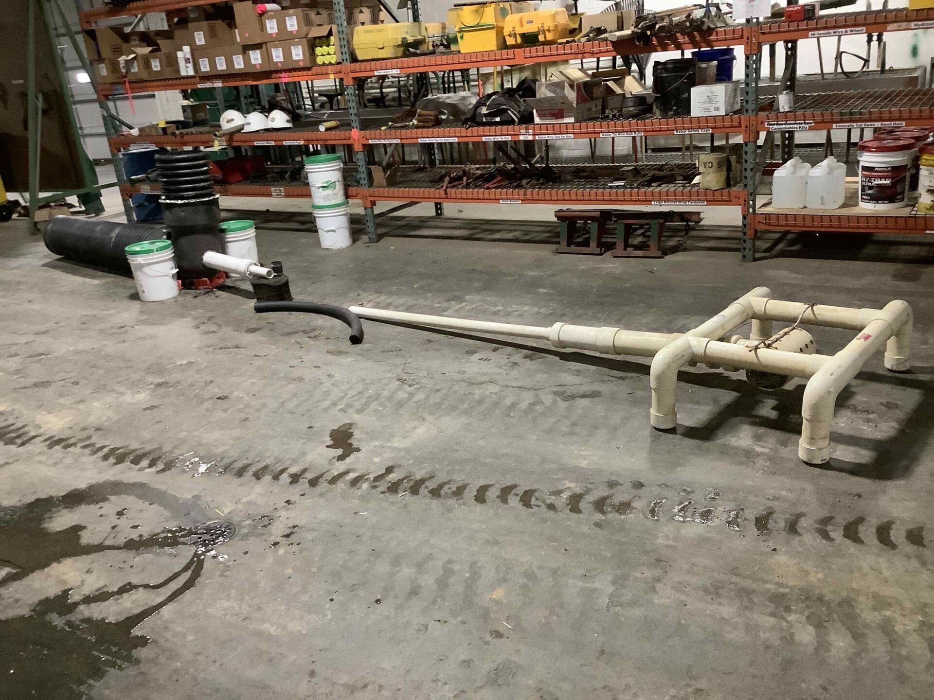 Workshop interior with a drainage system laid out on a concrete floor. Shelves with parts are in the background.
