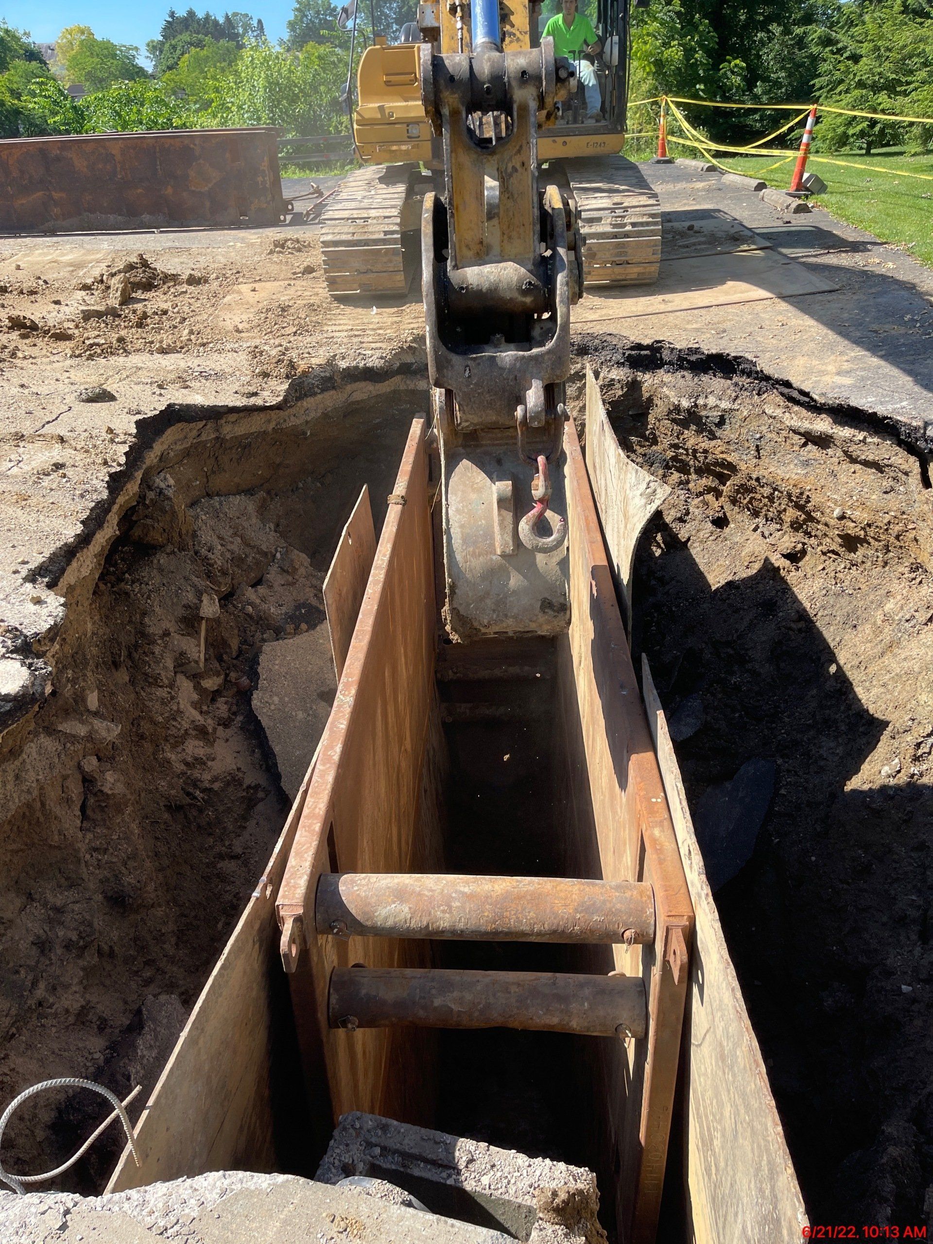 Excavator working in a trench supported by metal shoring; construction site.