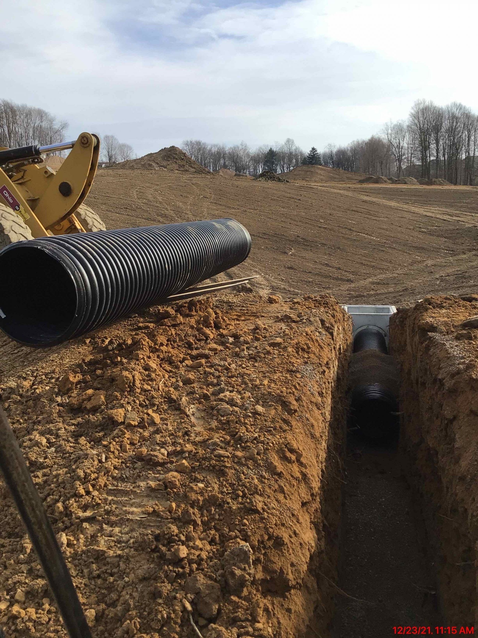A corrugated pipe lies near an open trench, construction site.