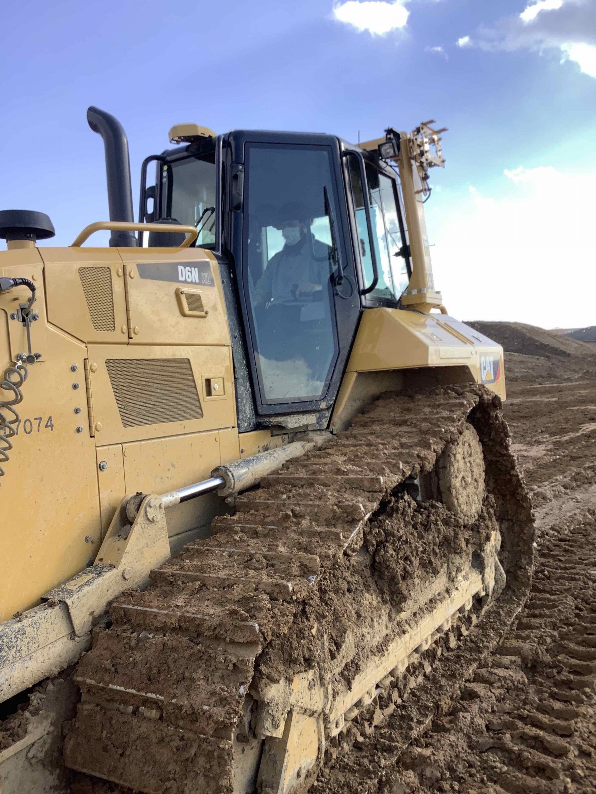 Yellow bulldozer on muddy ground with a clear sky, the operator is visible inside the cab.