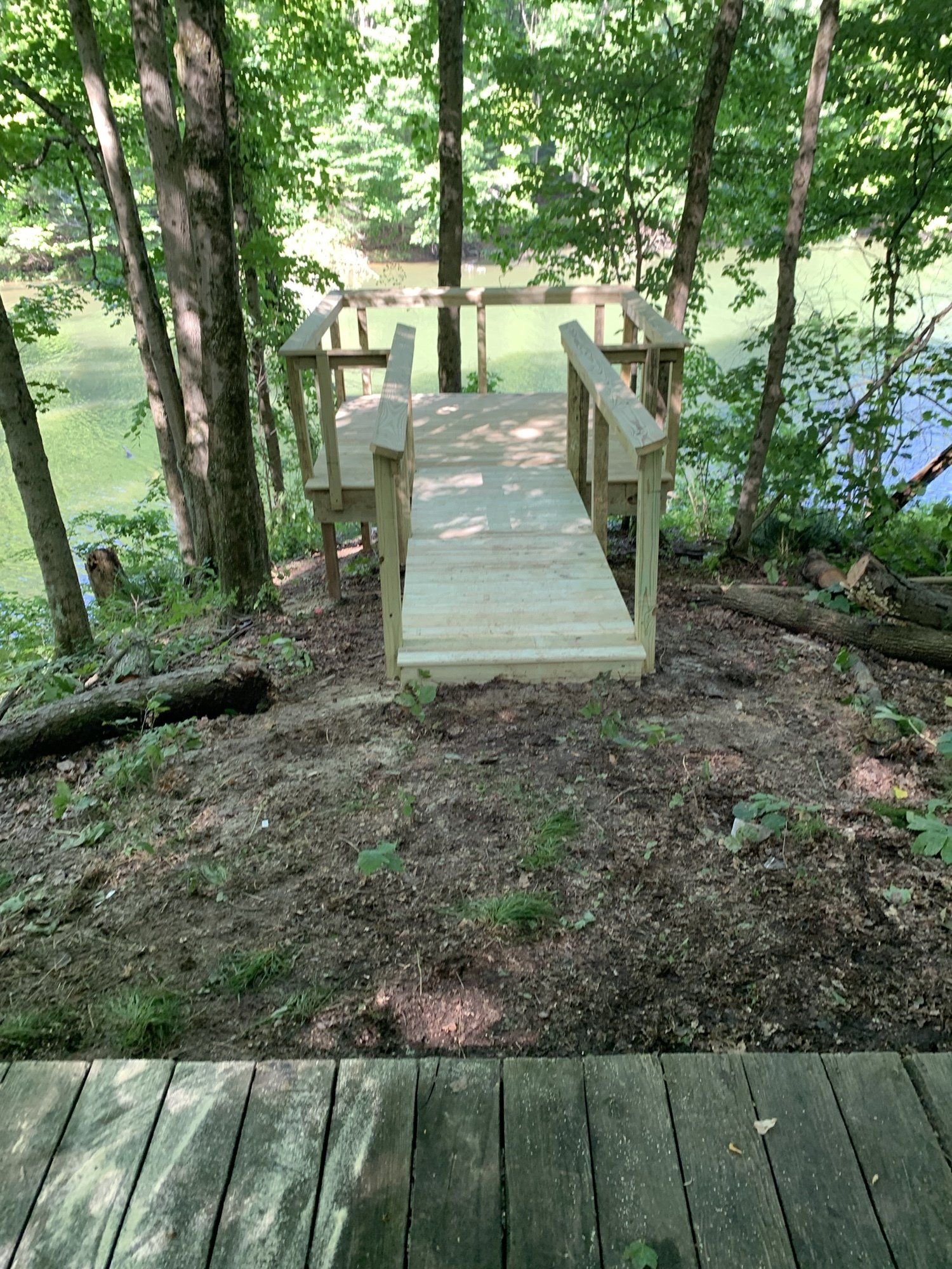 Wooden ramp leading down to a body of water, surrounded by trees and foliage.