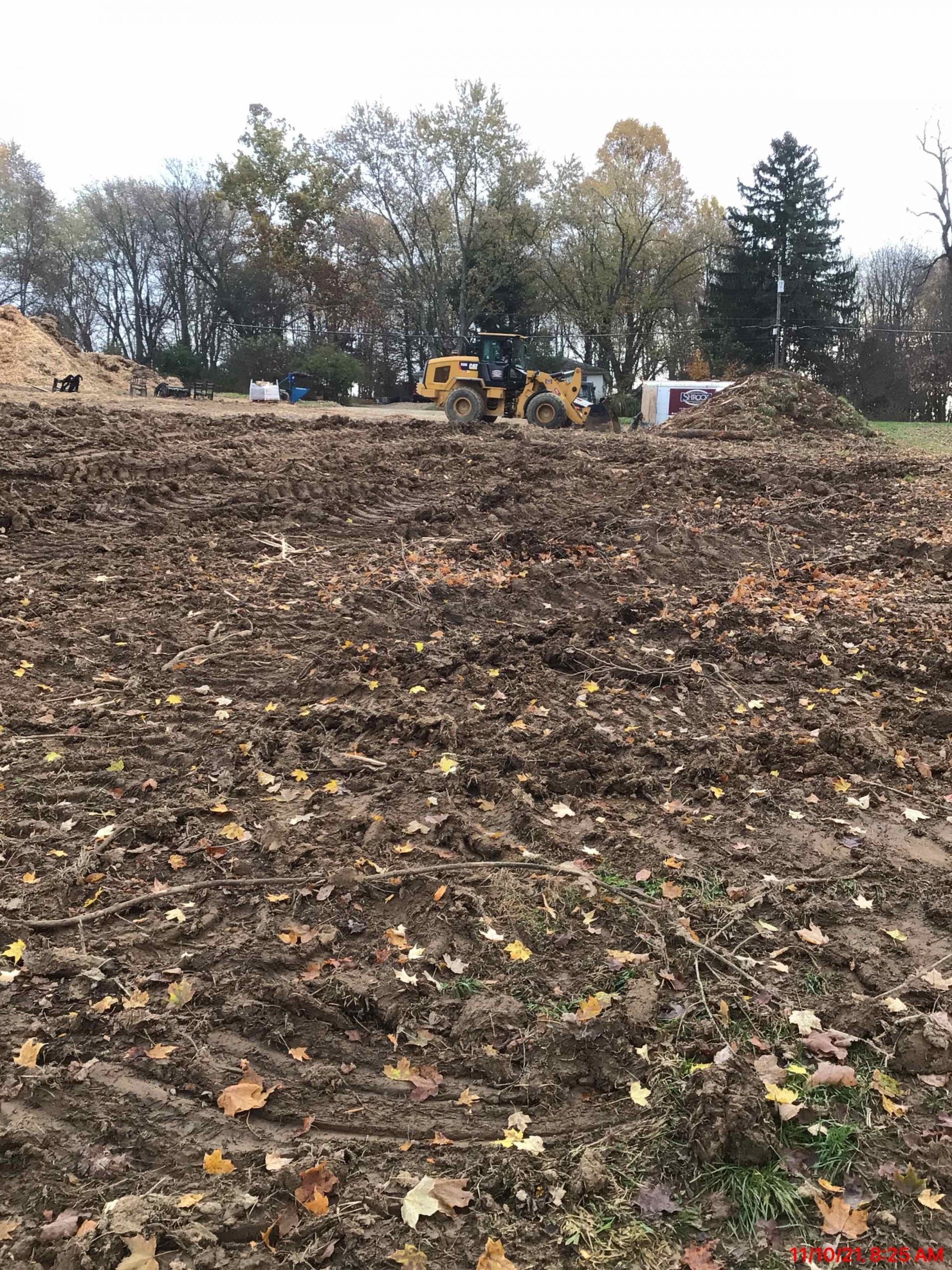 Muddy construction site with heavy machinery and trees in the background.