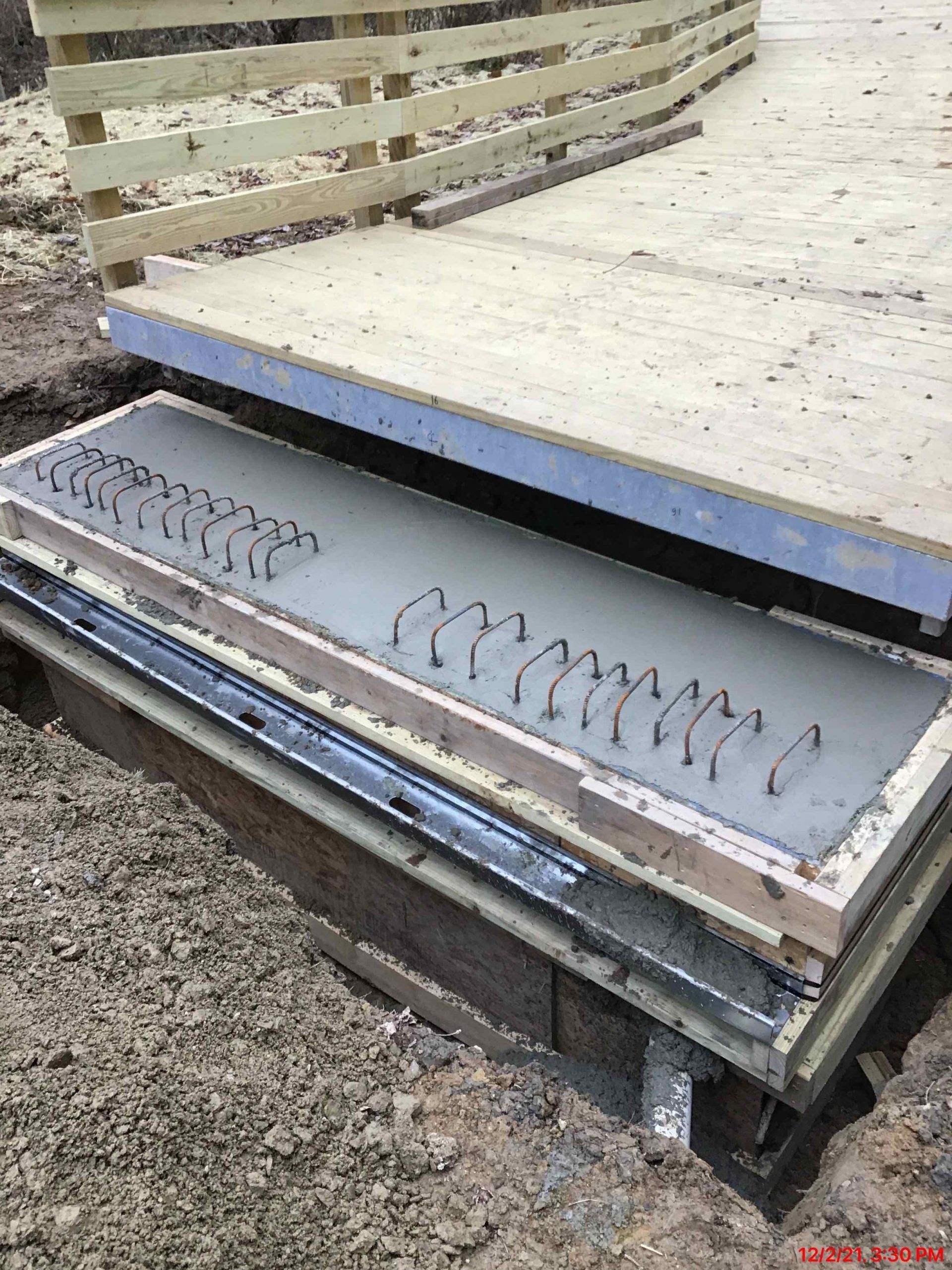 Concrete slab in a wooden frame with rebar, next to a wooden fence under construction.
