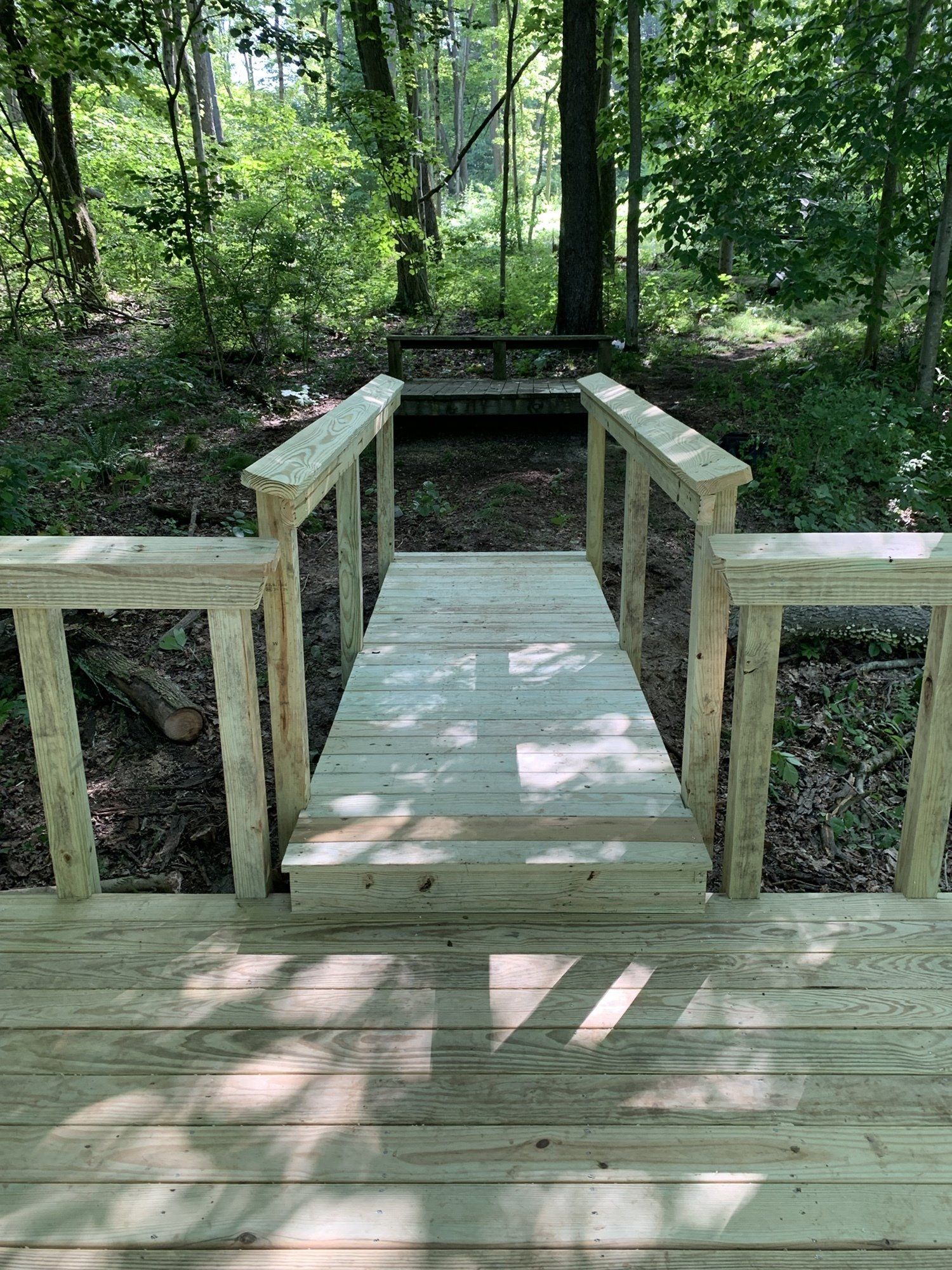 Wooden bridge over a small incline in a wooded area. The bridge has railings.