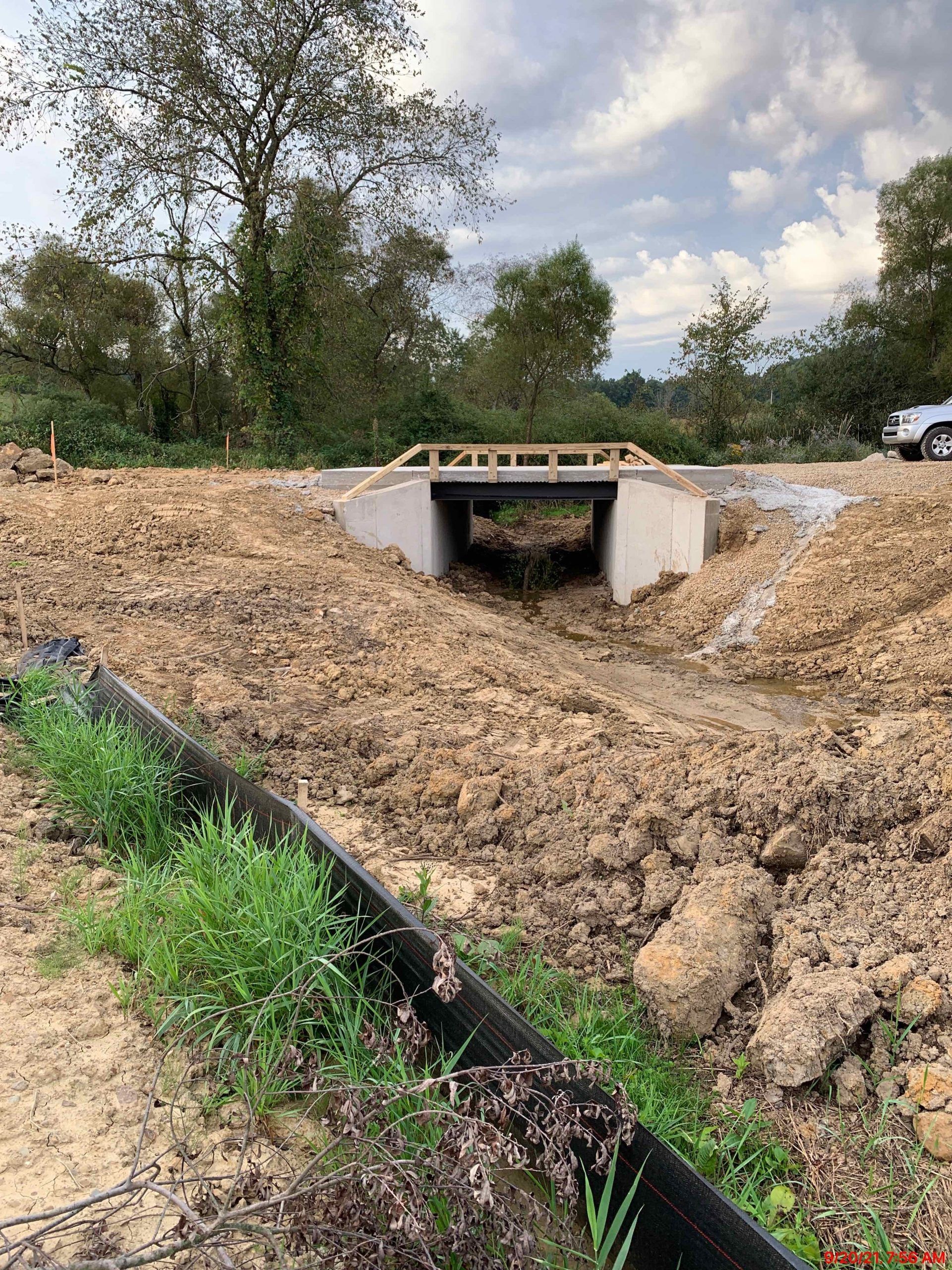 Construction site with a concrete bridge under a partially built wooden structure, with a muddy foreground.
