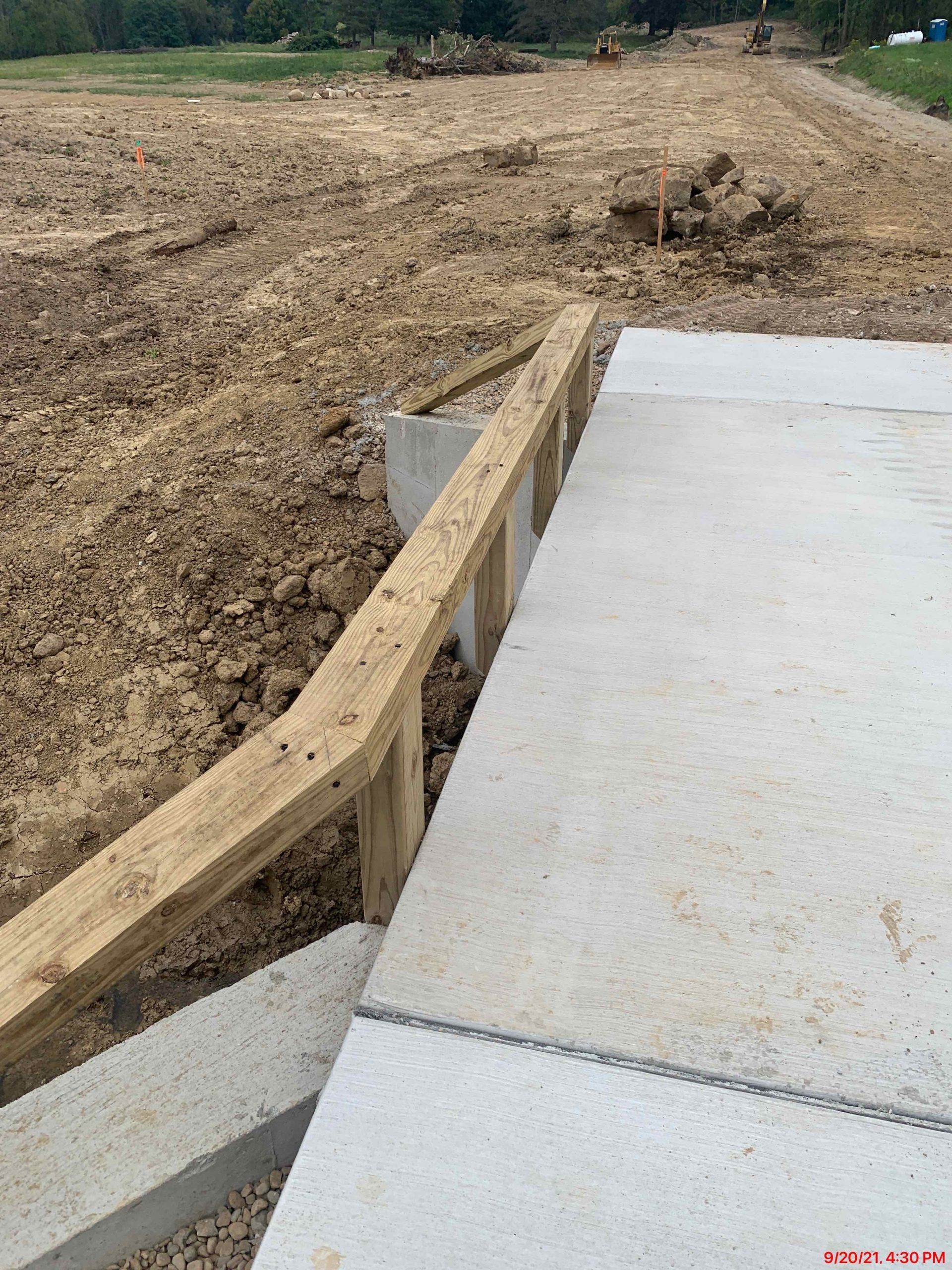 Wooden frame construction near concrete slabs and a dirt lot.