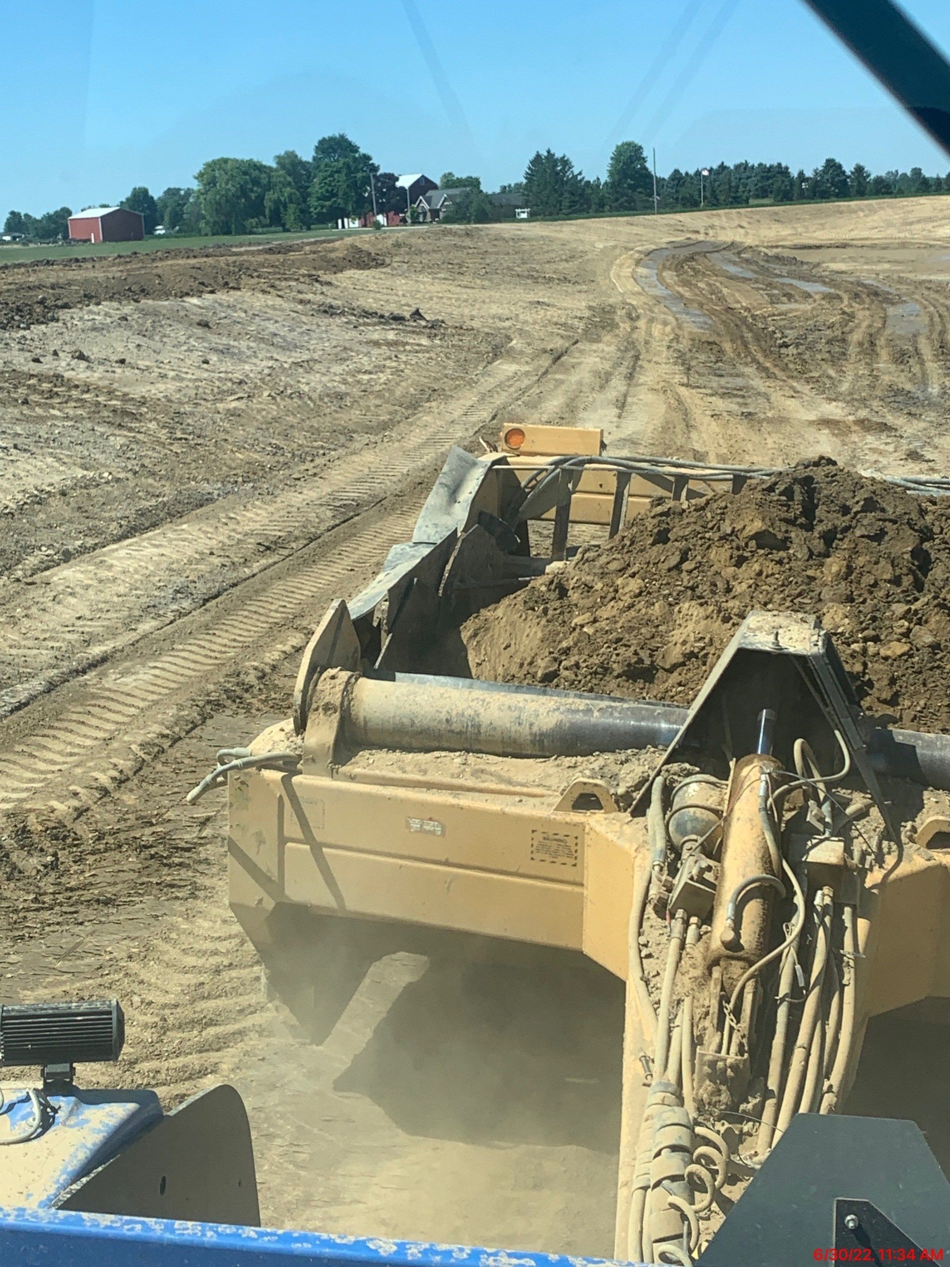 A bulldozer pushes dirt, creating a leveled area in a construction site with trees and buildings visible.