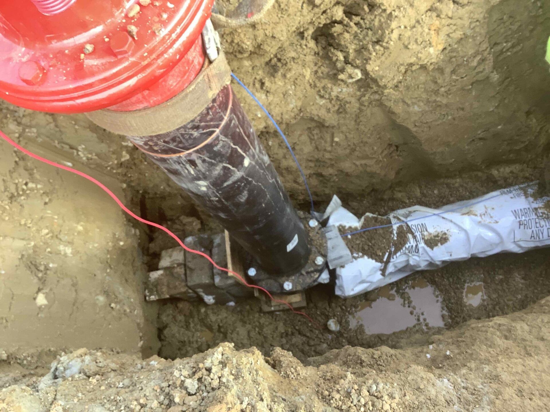 A buried water pipe joint repair in a trench, red fire hydrant, wires and soil.