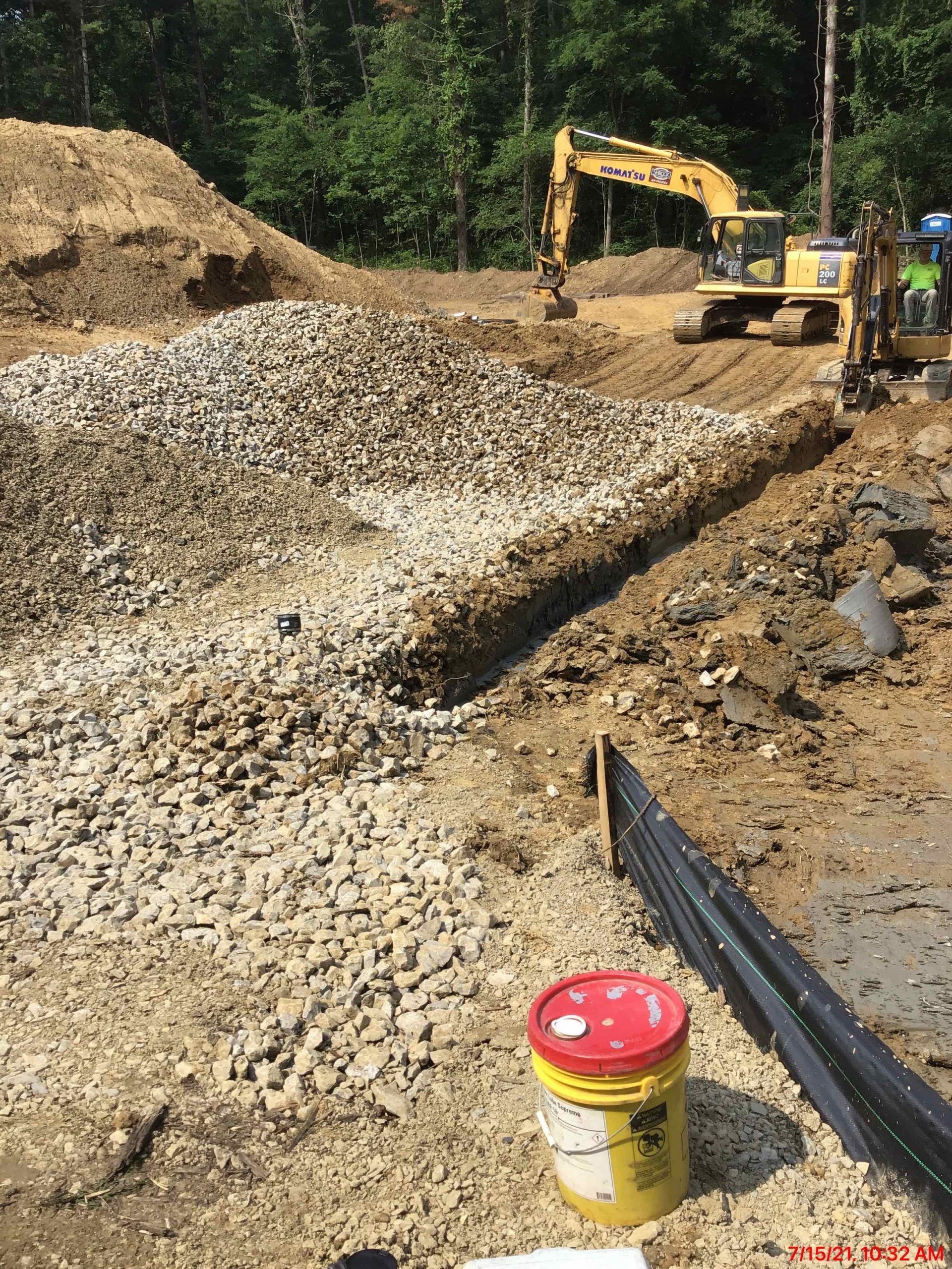 Construction site: Excavator digging, gravel pile, dirt, and a bucket.