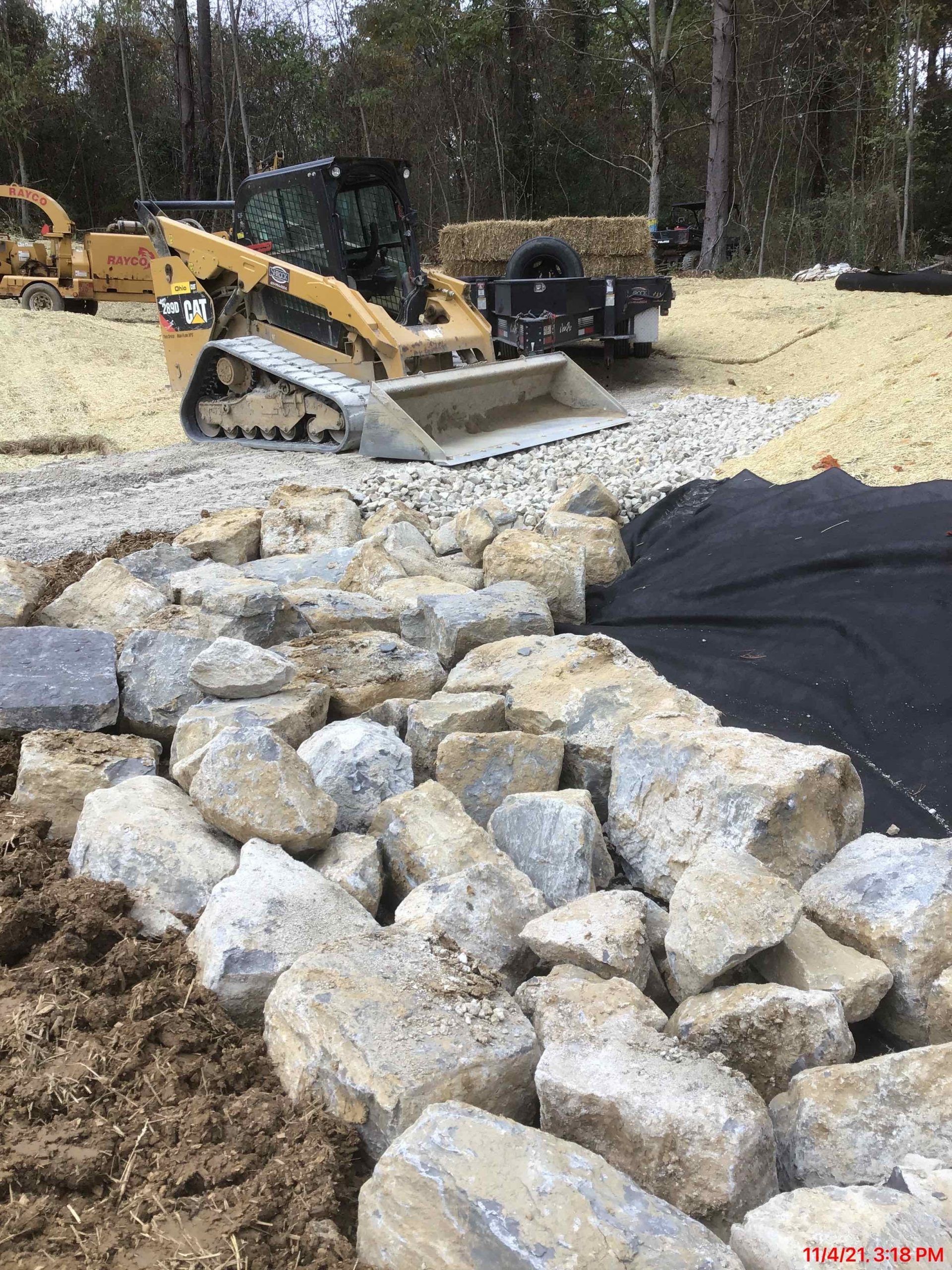 Skid steer loader placing rocks for retaining wall on a construction site.