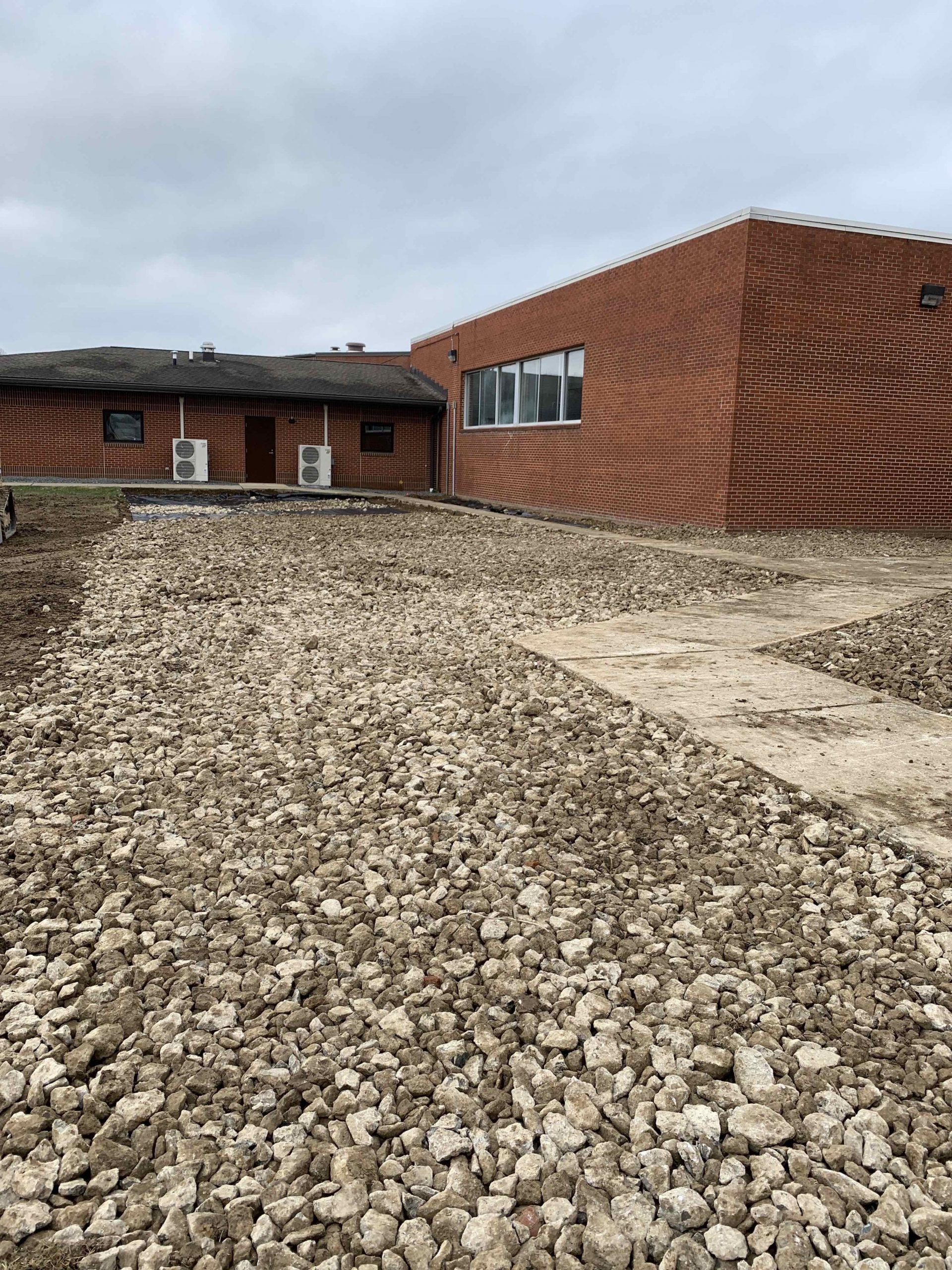Gravel pathway leading to red brick buildings with windows under a cloudy sky.