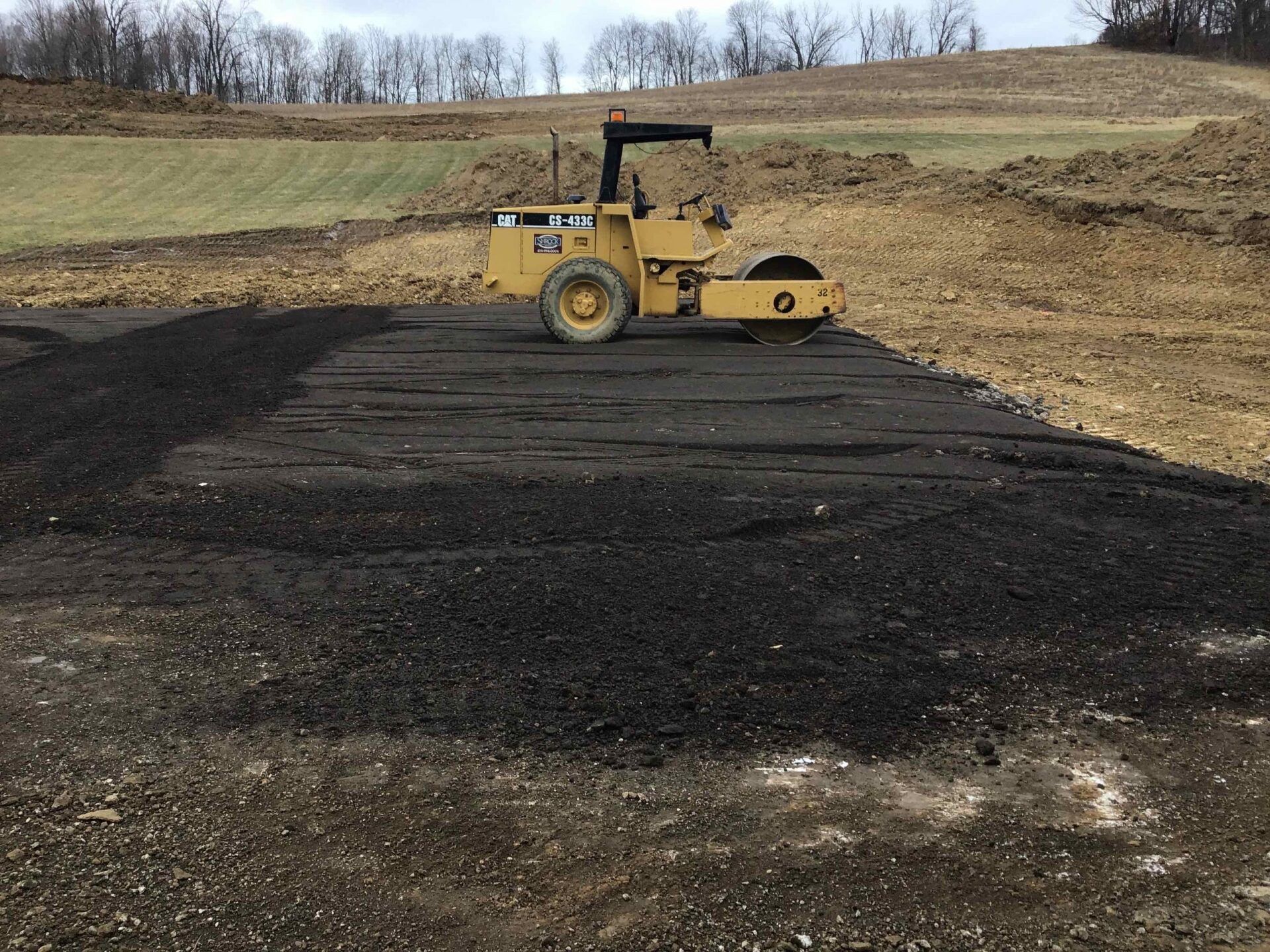 Yellow road roller compacting dark gravel on a construction site.