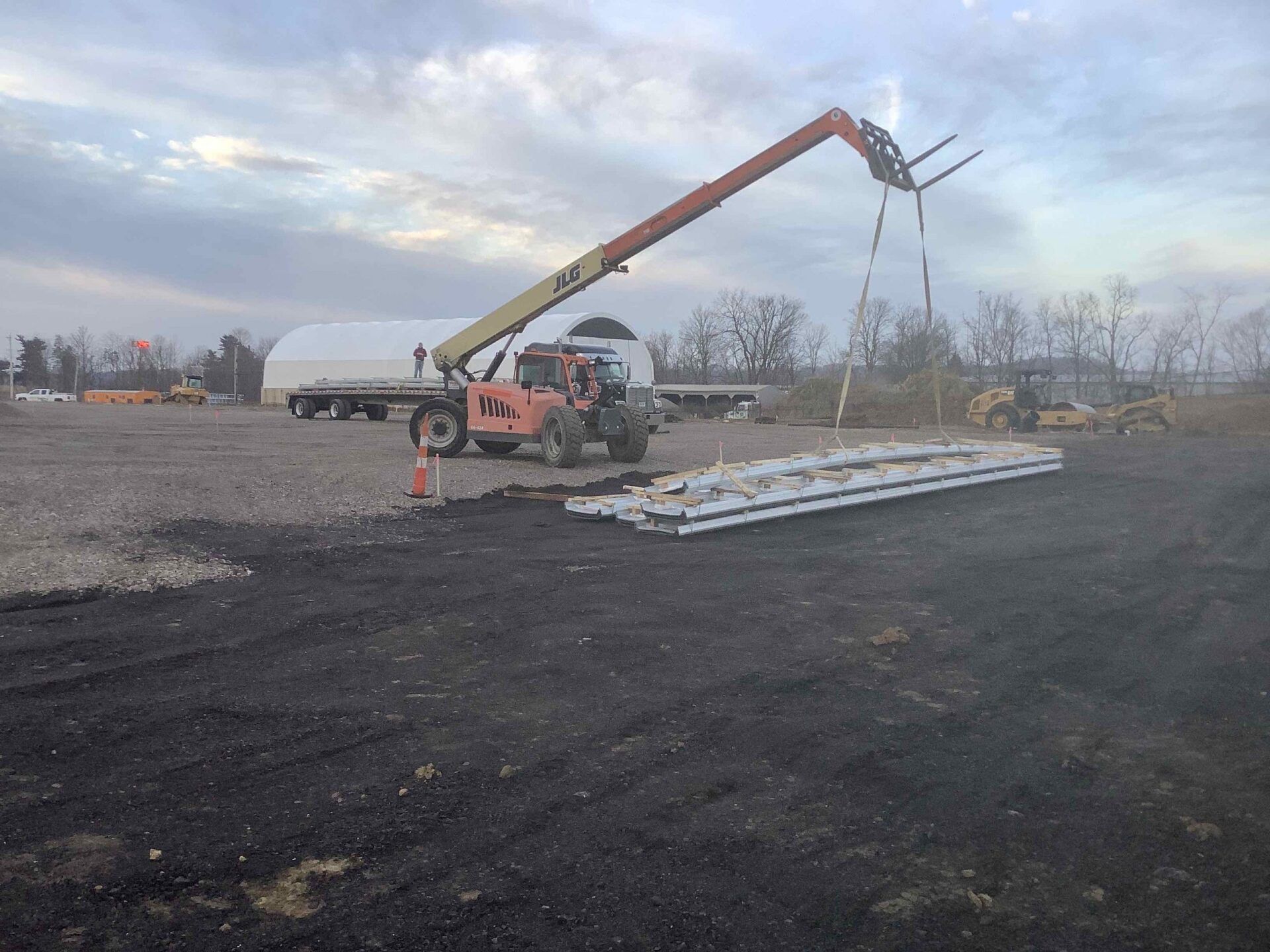 Forklift lifting beams on a construction site; overcast sky.