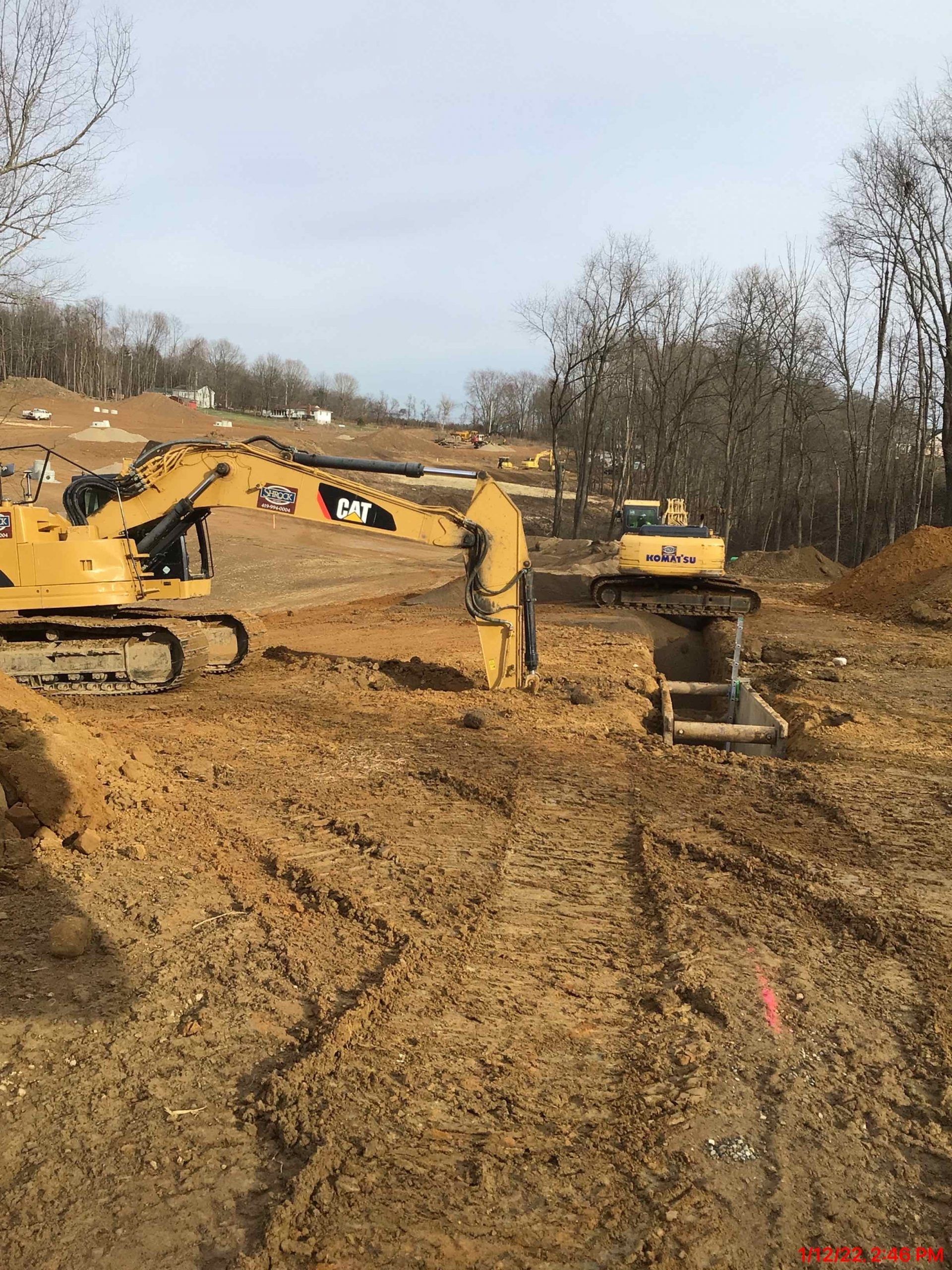 Two yellow excavators on a muddy construction site, clearing land on a cloudy day.