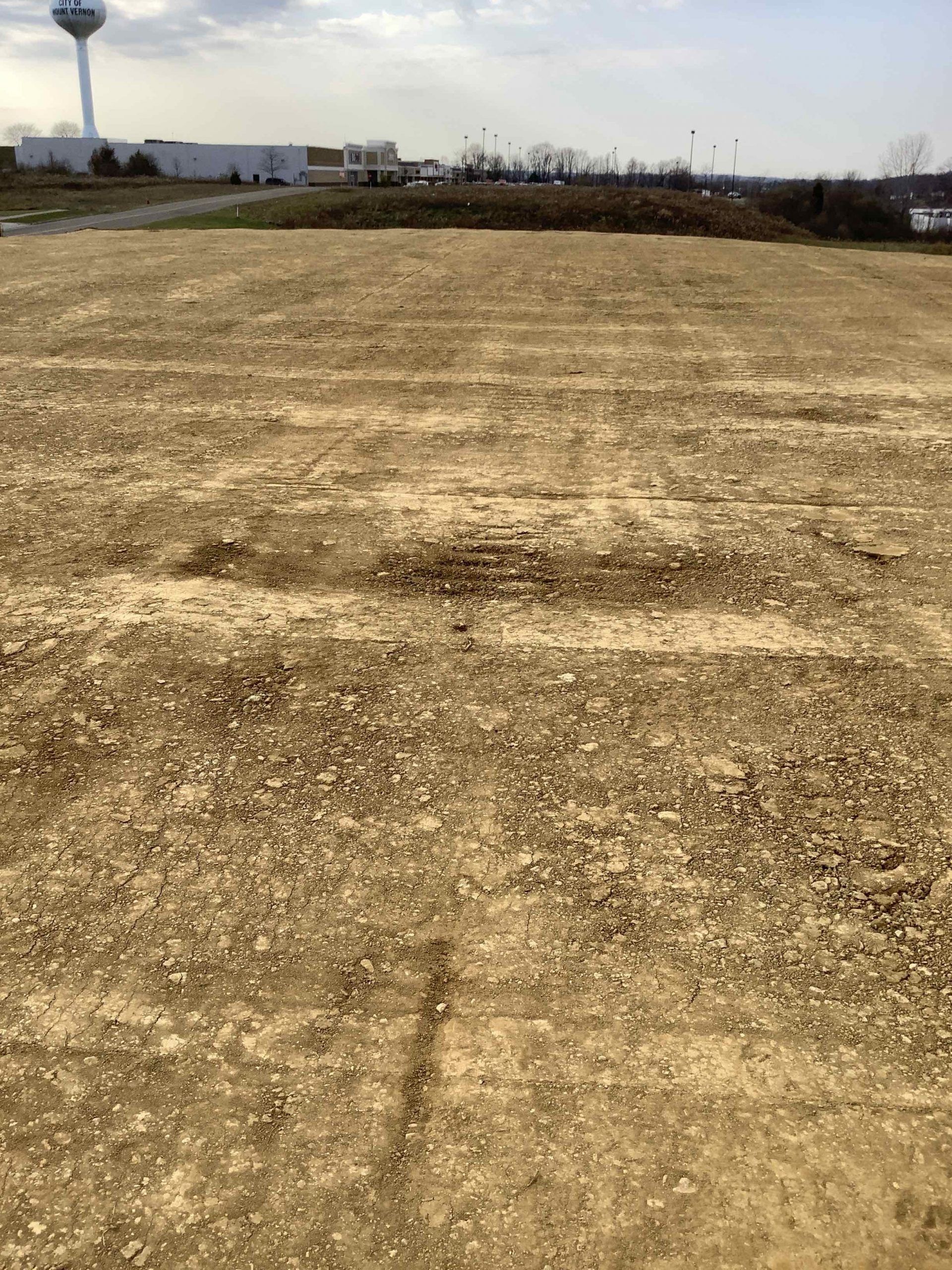 Dirt lot with visible tire tracks, water tower and distant buildings. Overcast sky.