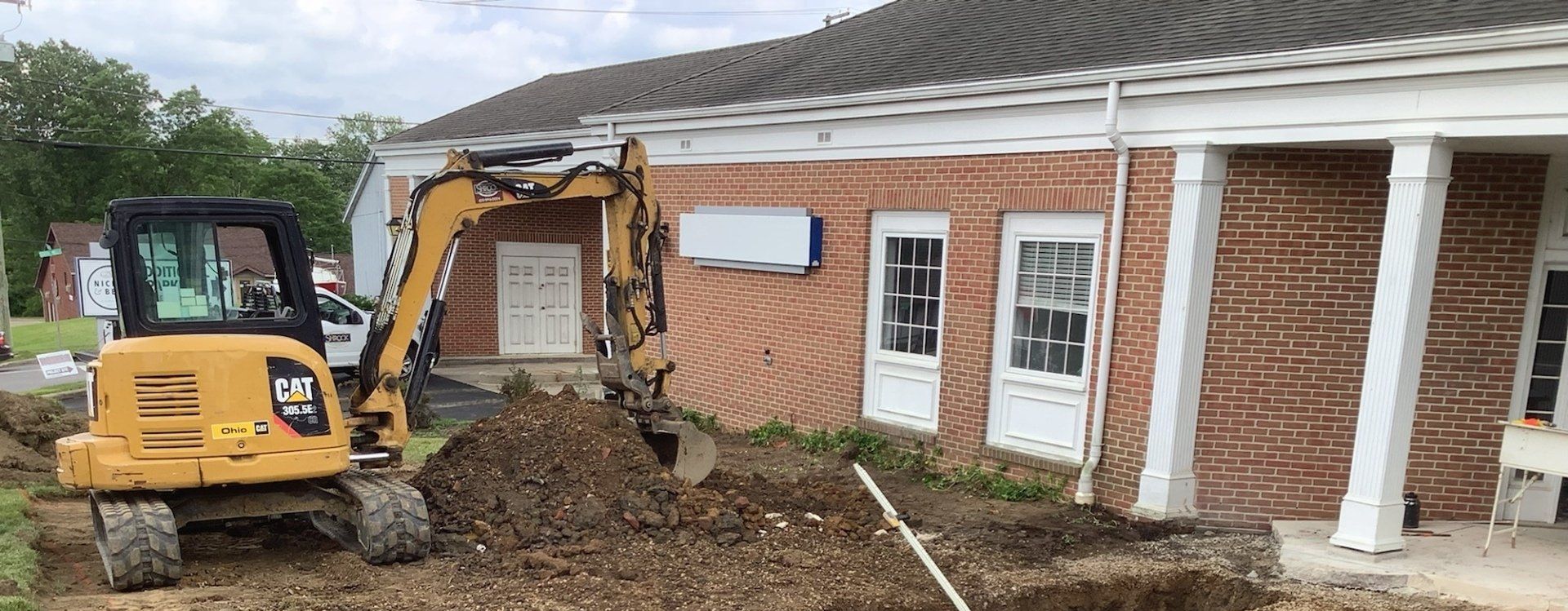 Yellow excavator digging near a red brick building with white pillars and windows.