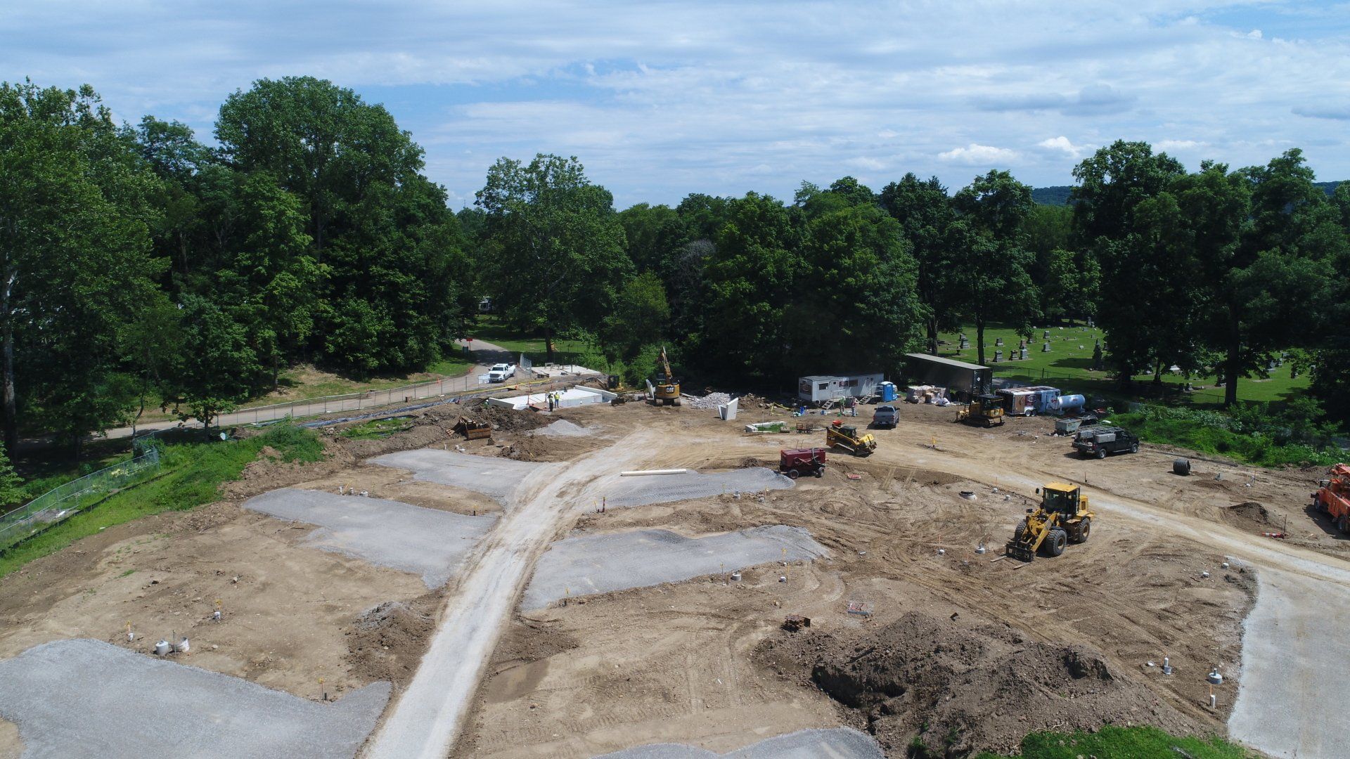 Aerial view of a construction site in a park. Heavy machinery is working on the dirt and cleared areas.