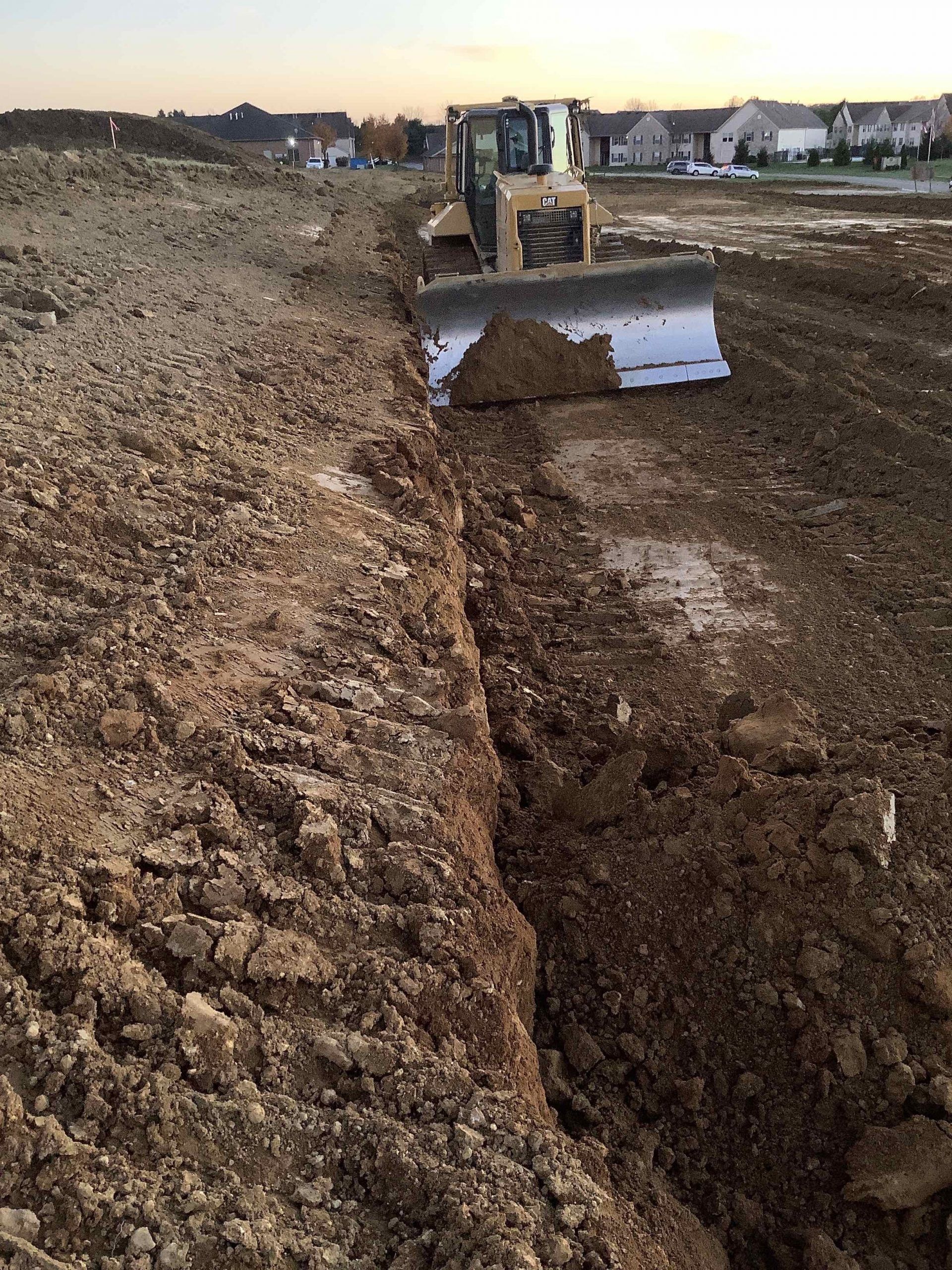 Bulldozer grading a construction site, pushing dirt. Houses in the background.