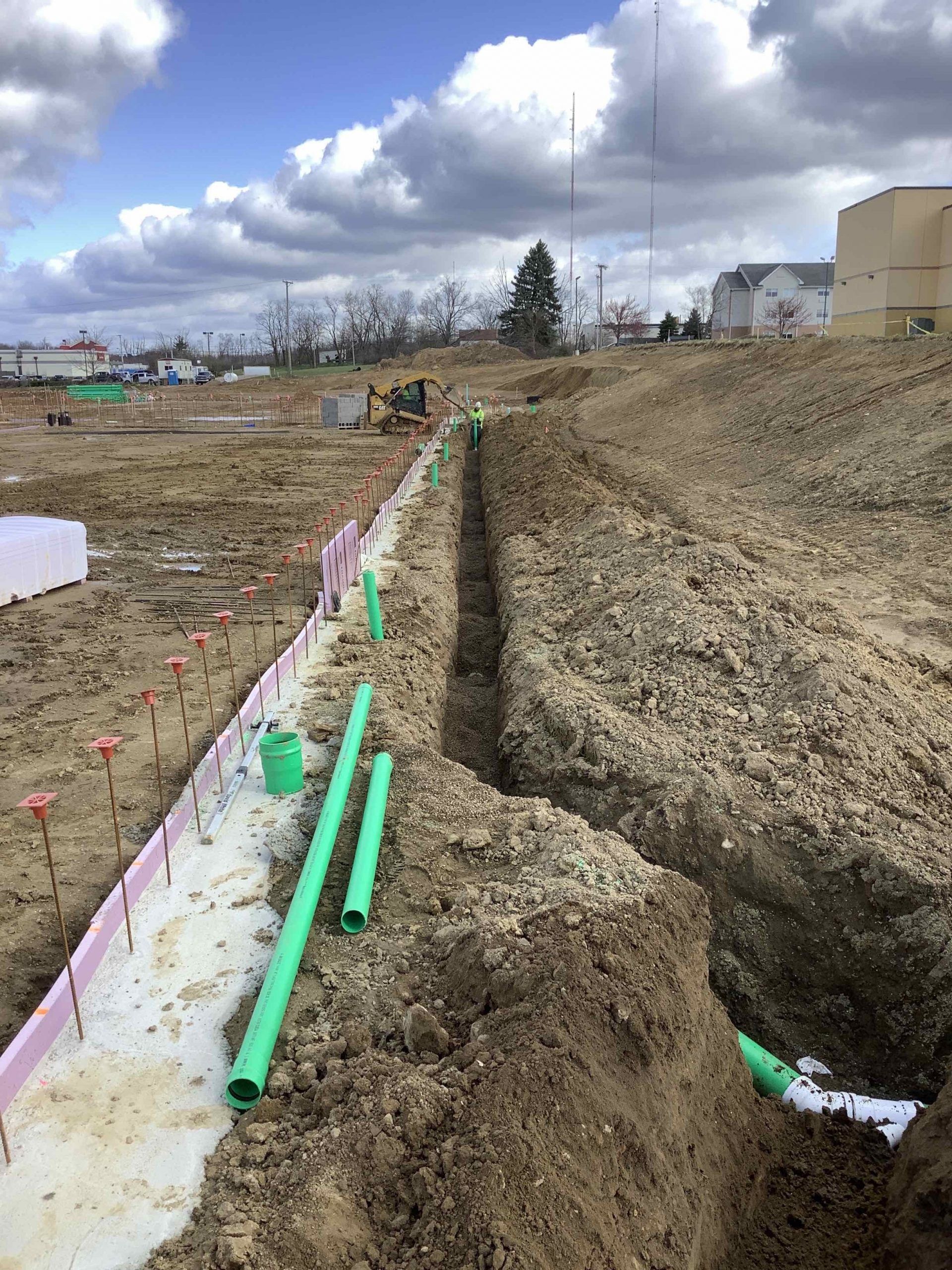 Construction site with a trench, green pipes, and dirt.