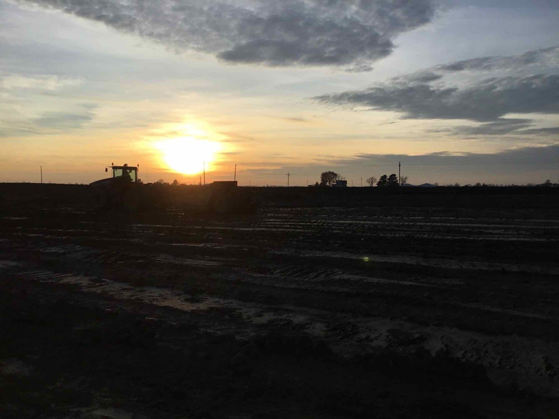 Sunrise over a muddy field with a tractor silhouetted against the bright sun.