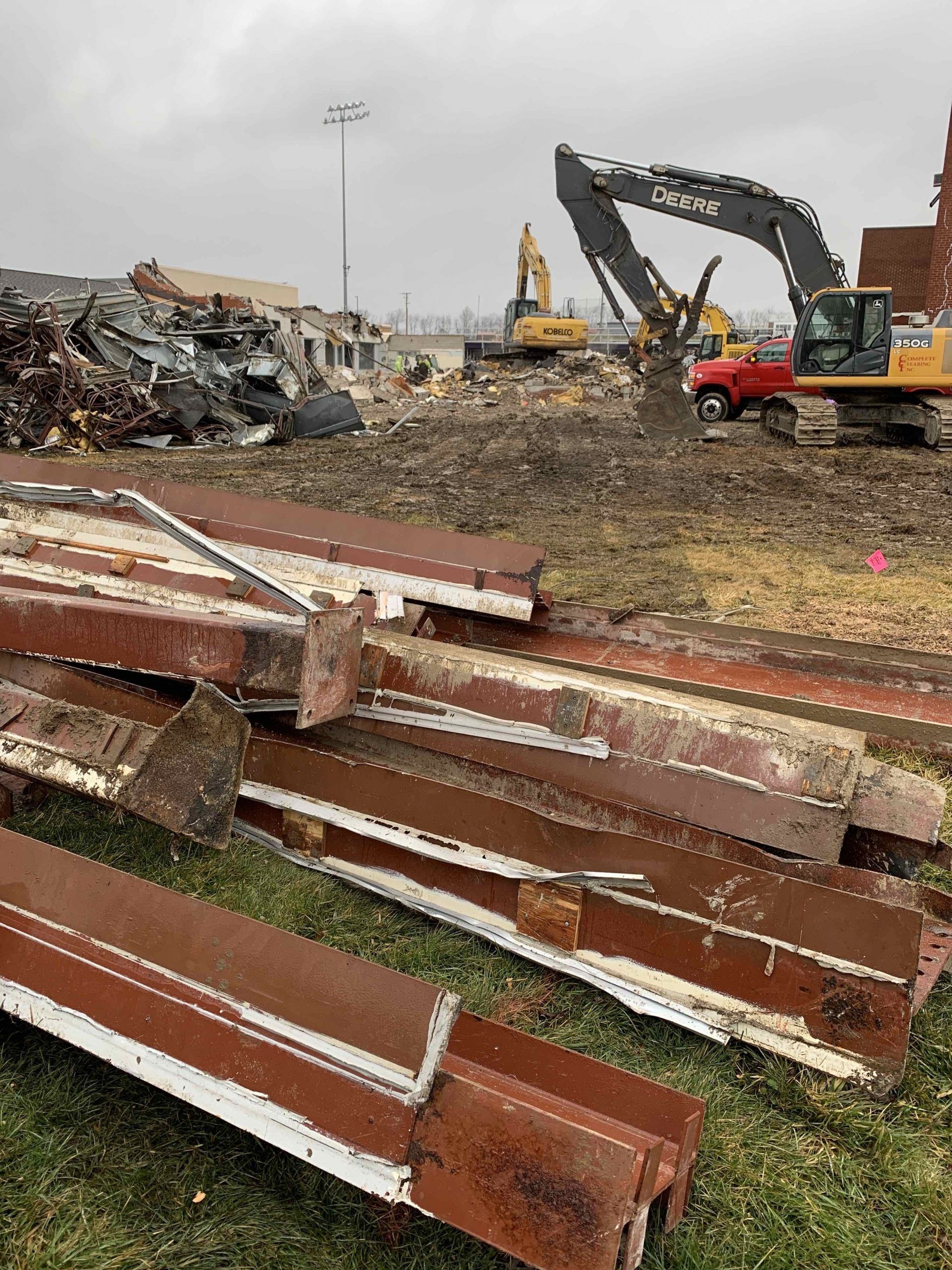 Demolition site with piles of rusted metal beams and excavators on a cloudy day.
