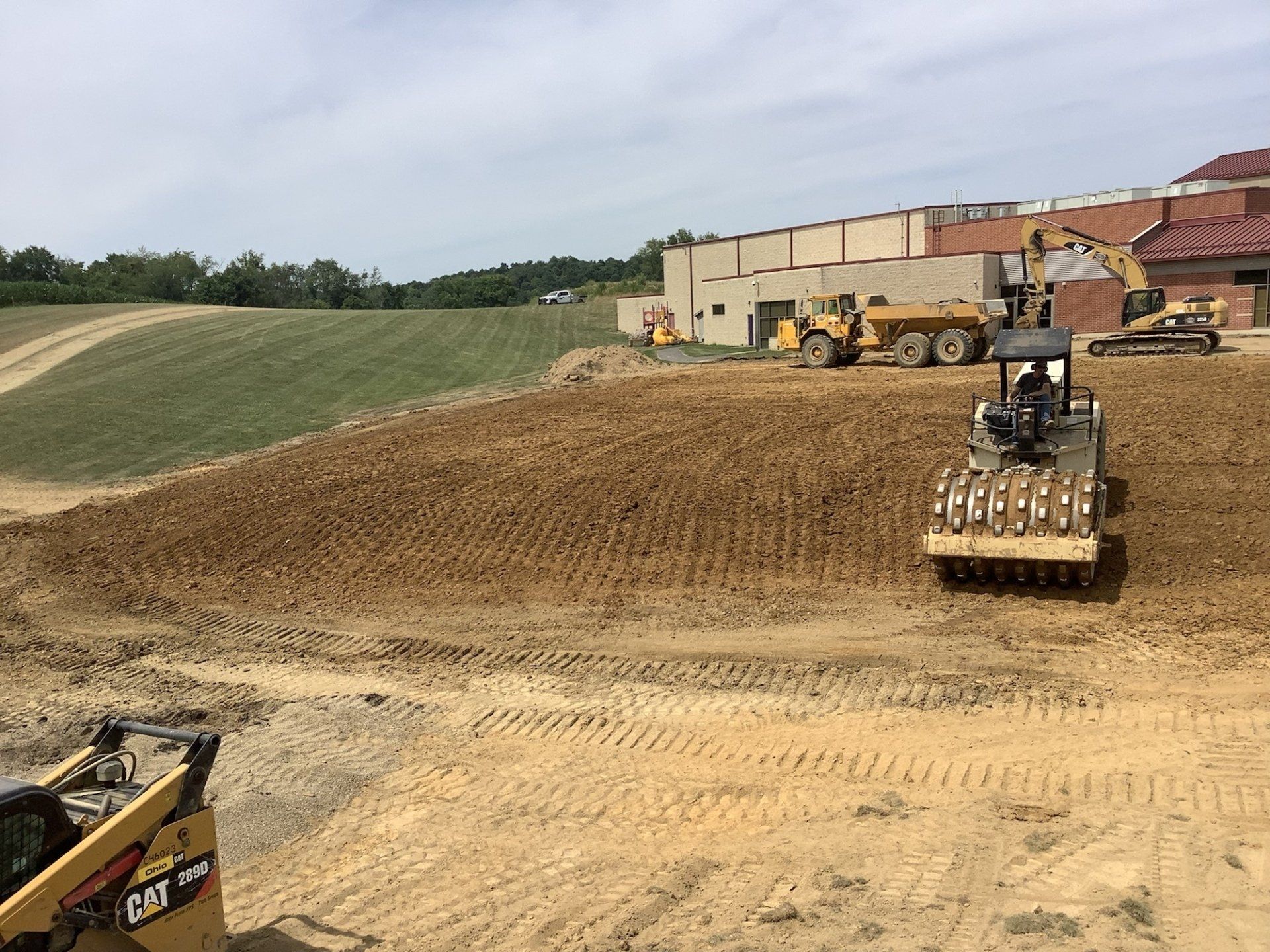 Construction site with a soil compactor, earthmovers, and a building under construction.