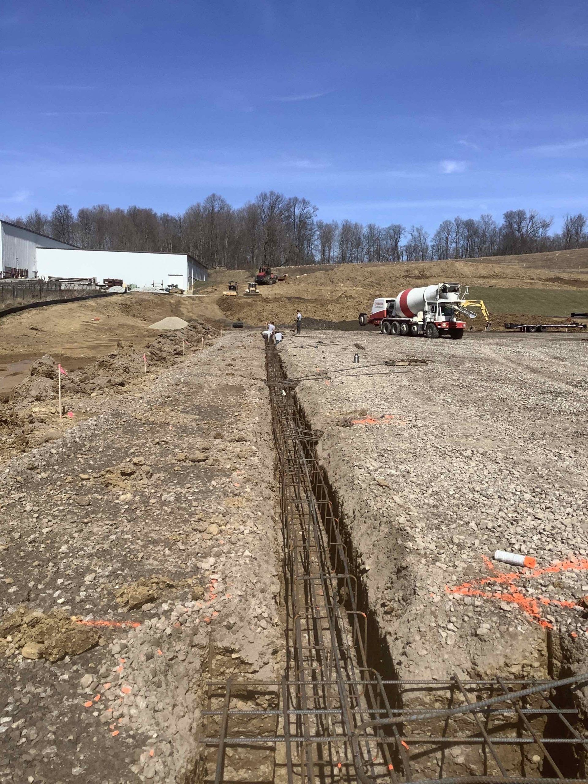 Construction site with rebar in a trench, concrete truck in the background, blue sky.