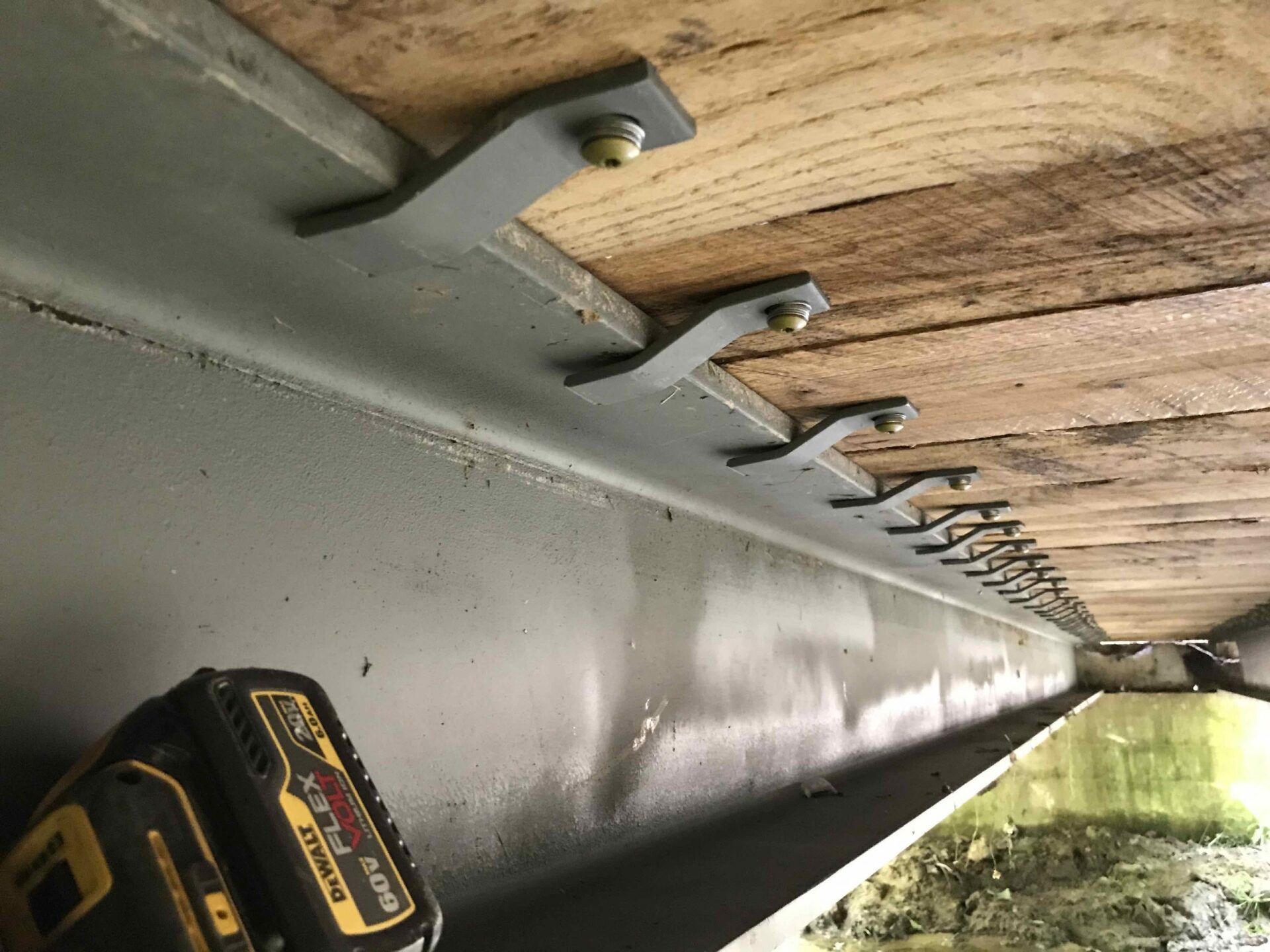 Metal brackets securing wooden planks to a gray beam; a drill sits below.