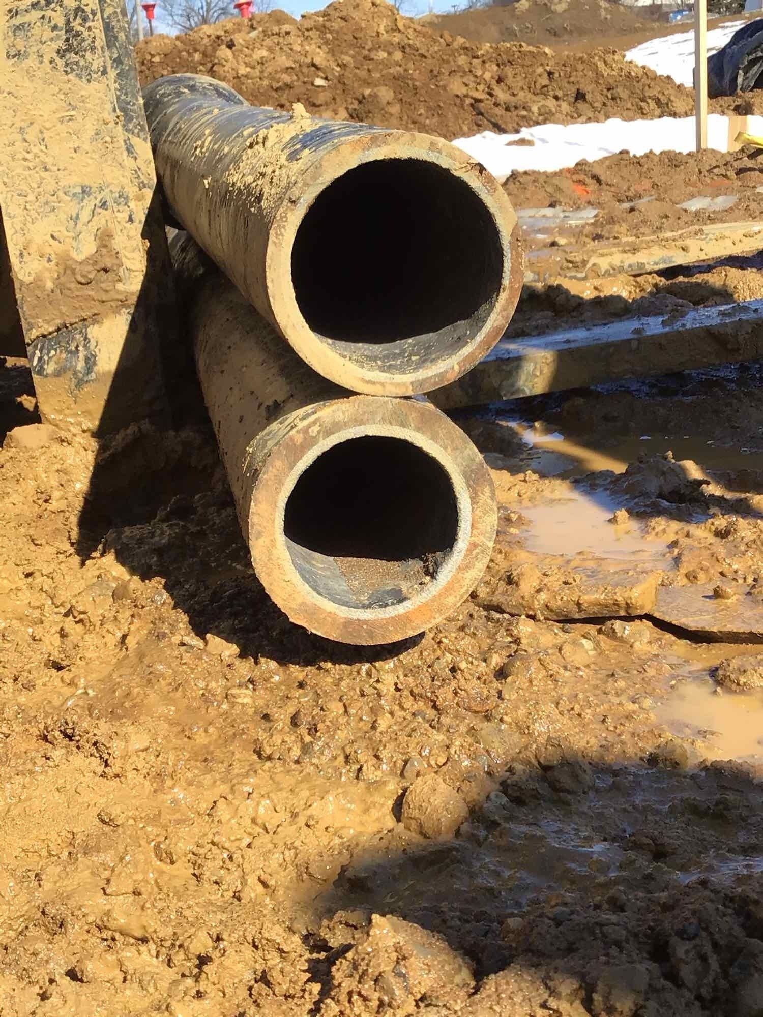 Two large, muddy pipes in a construction site with brown mud and dirt.
