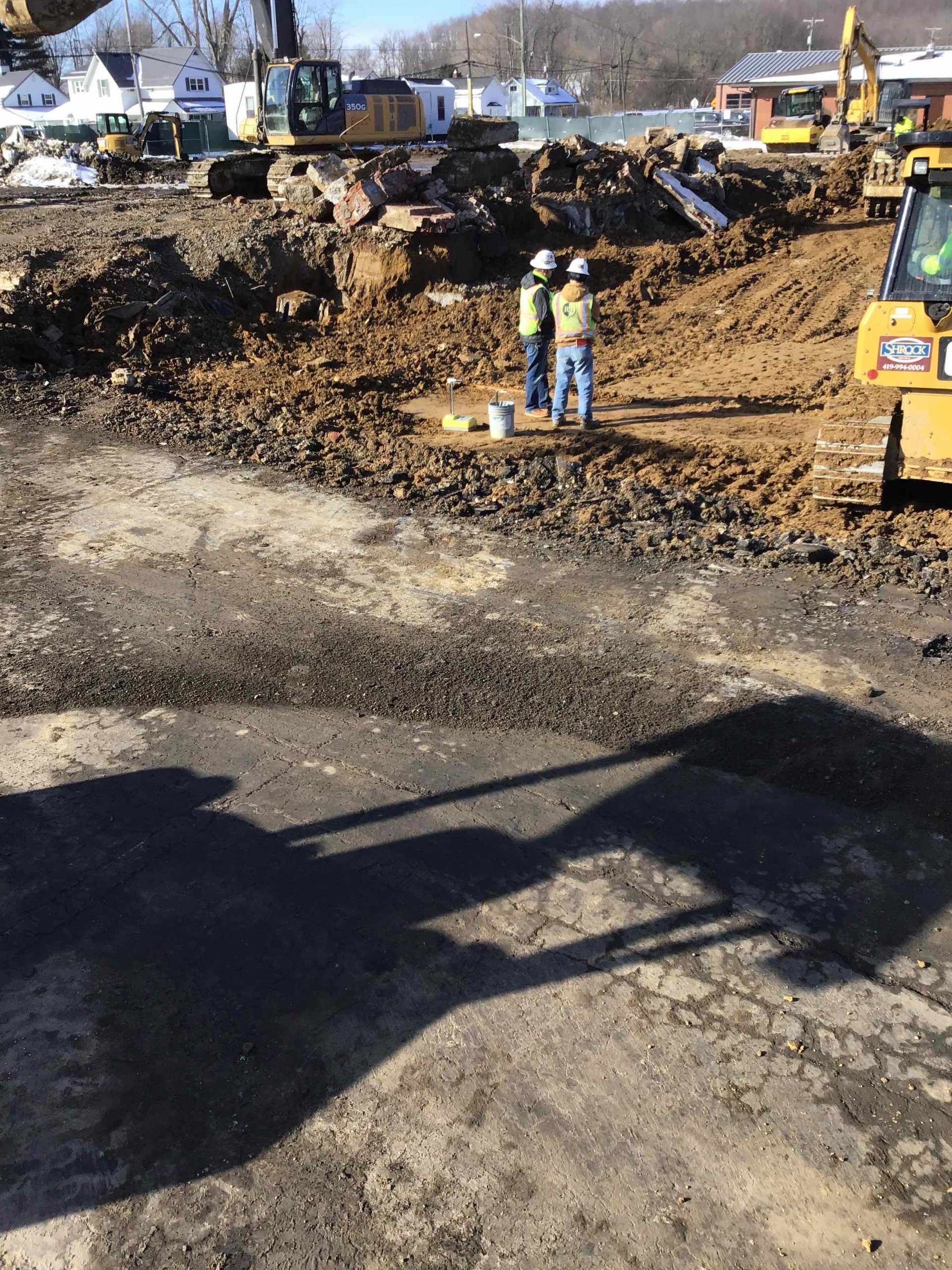 Construction site with two workers in safety vests; excavators and dirt piles.