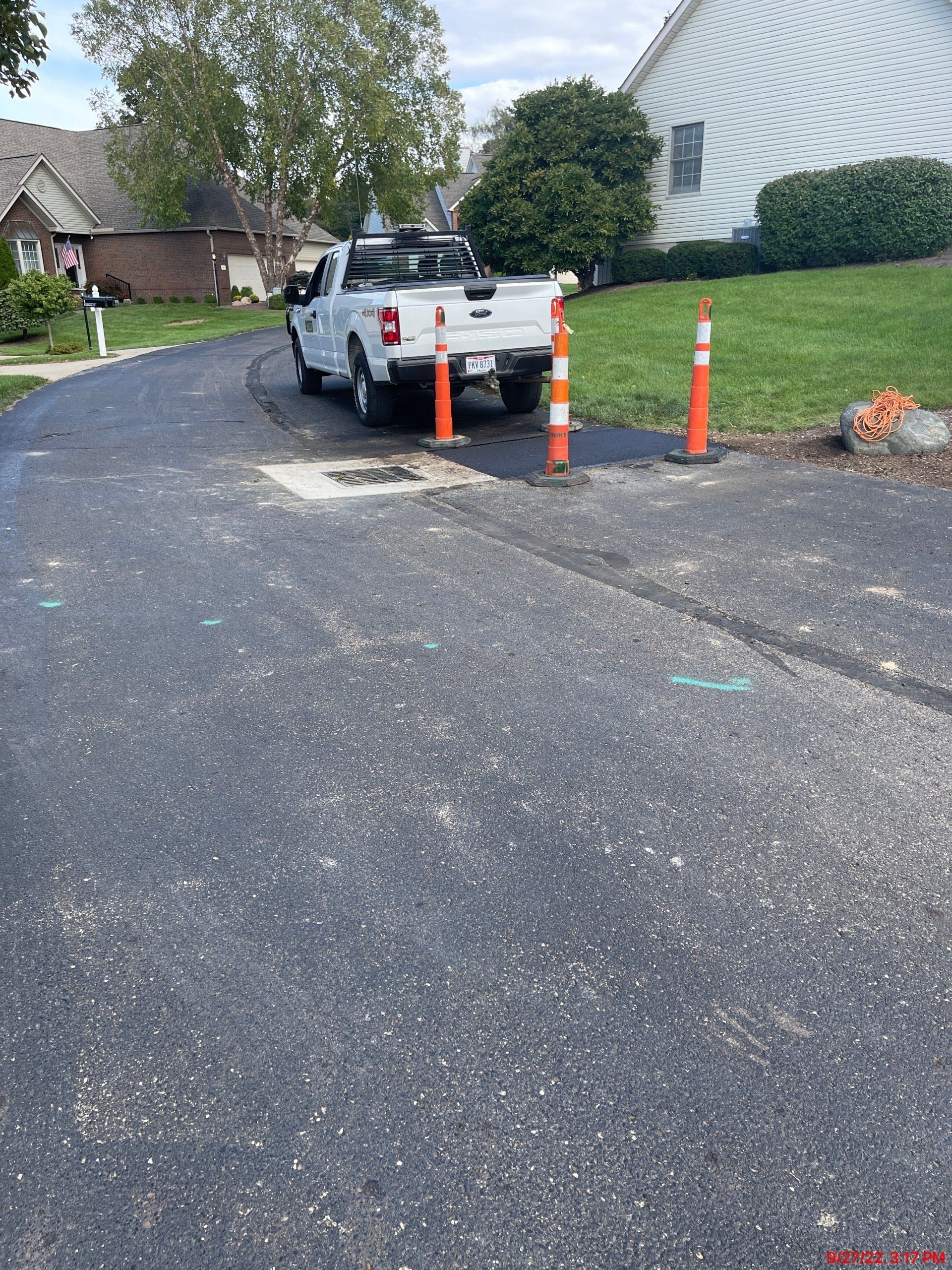 White truck parked on freshly paved asphalt, orange traffic cones.