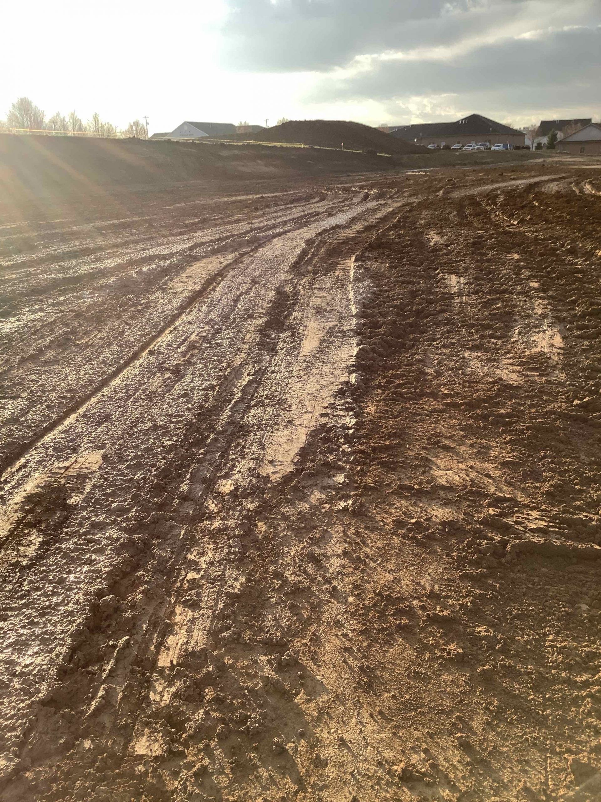 Muddy construction site under a partly cloudy sky, with sun shining.
